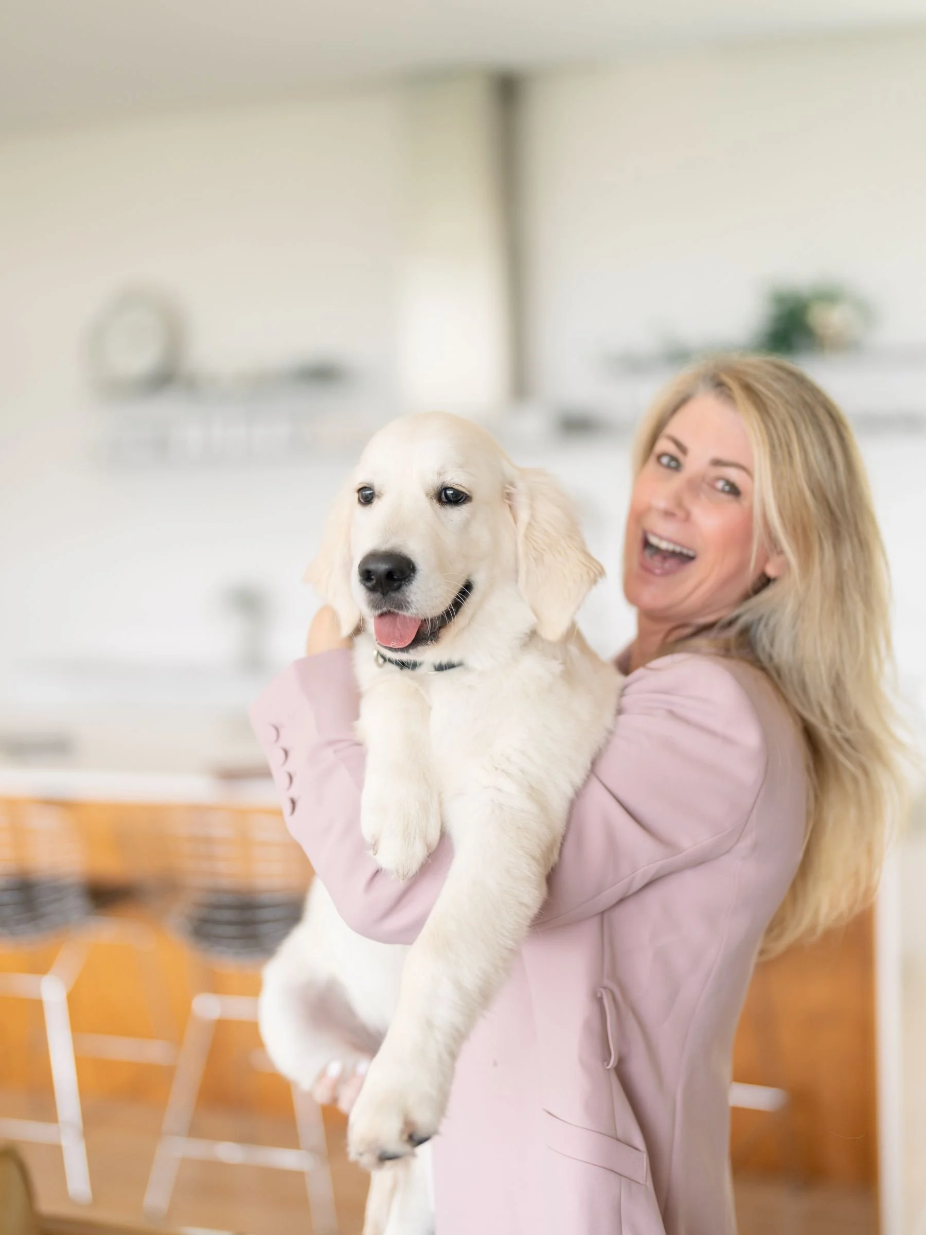 A woman holding a happy Golden Retriever puppy inside a bright, modern room.