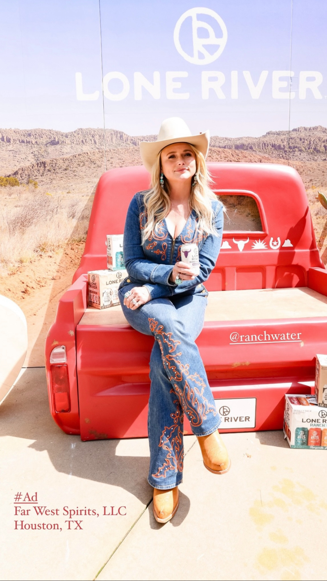 A woman with blonde hair wearing a white cowboy hat, blue embroidered jeans, and orange cowboy boots, sitting on the back of a red pickup truck in a desert landscape with mountains in the background. She is holding a can of Lone River Ranch Water. Be