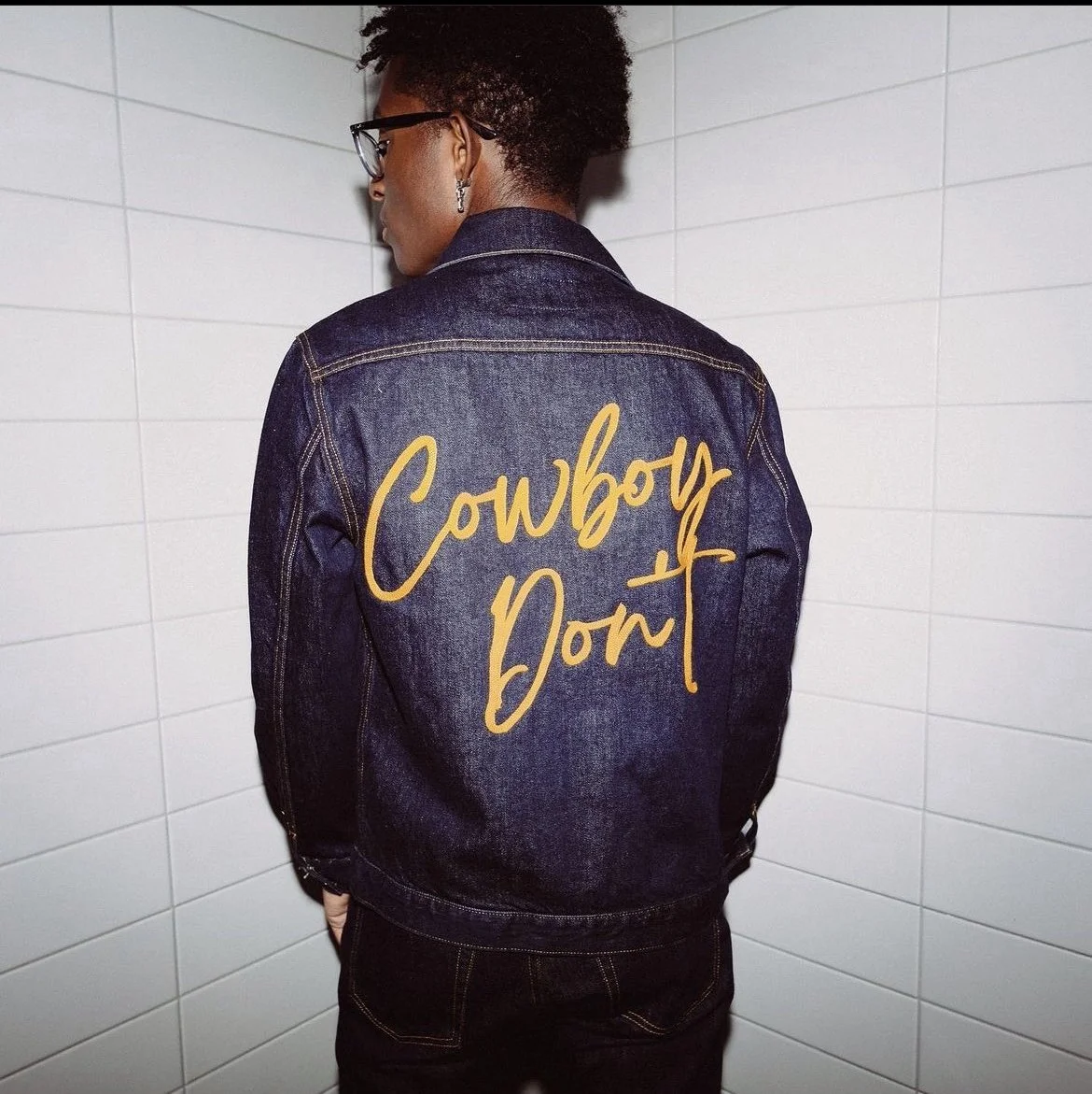 Back of a person wearing a denim jacket with yellow cursive text that says "Cowboy Don".