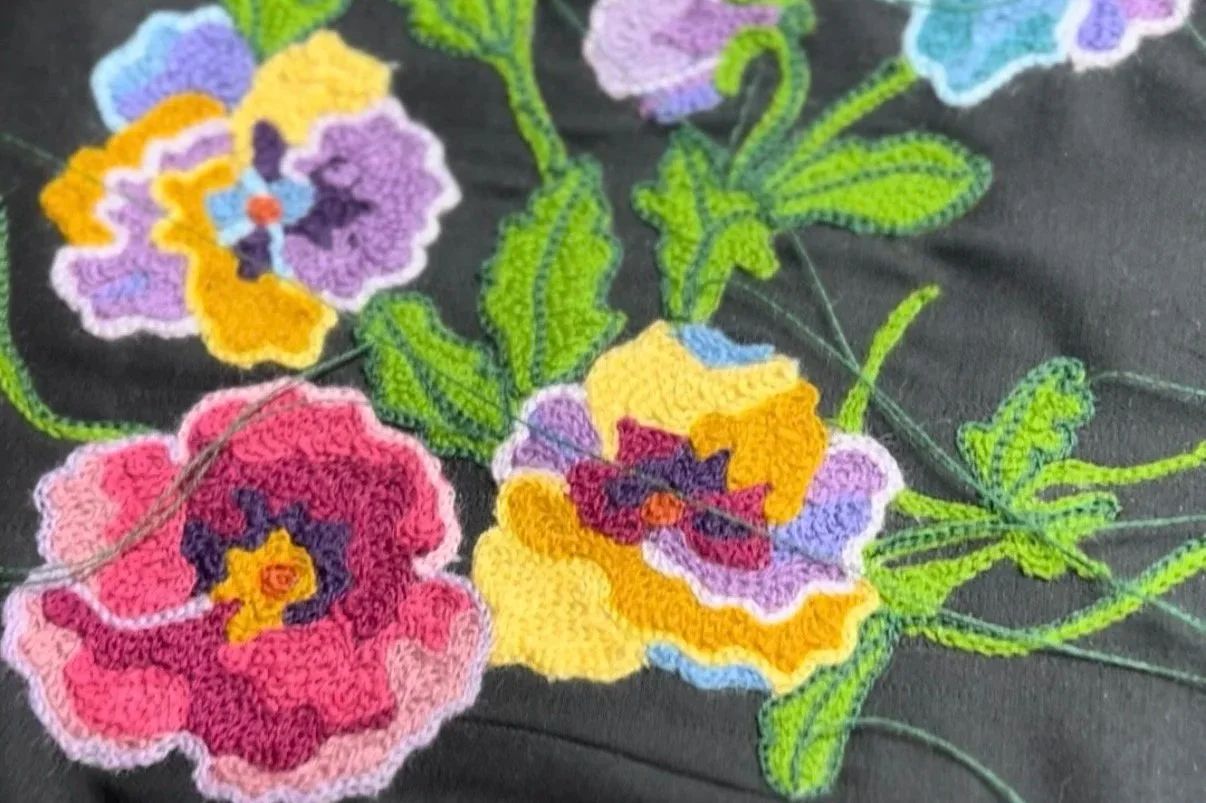 Colorful embroidered floral chainstitch on black fabric with pink, purple, yellow, and green thread.