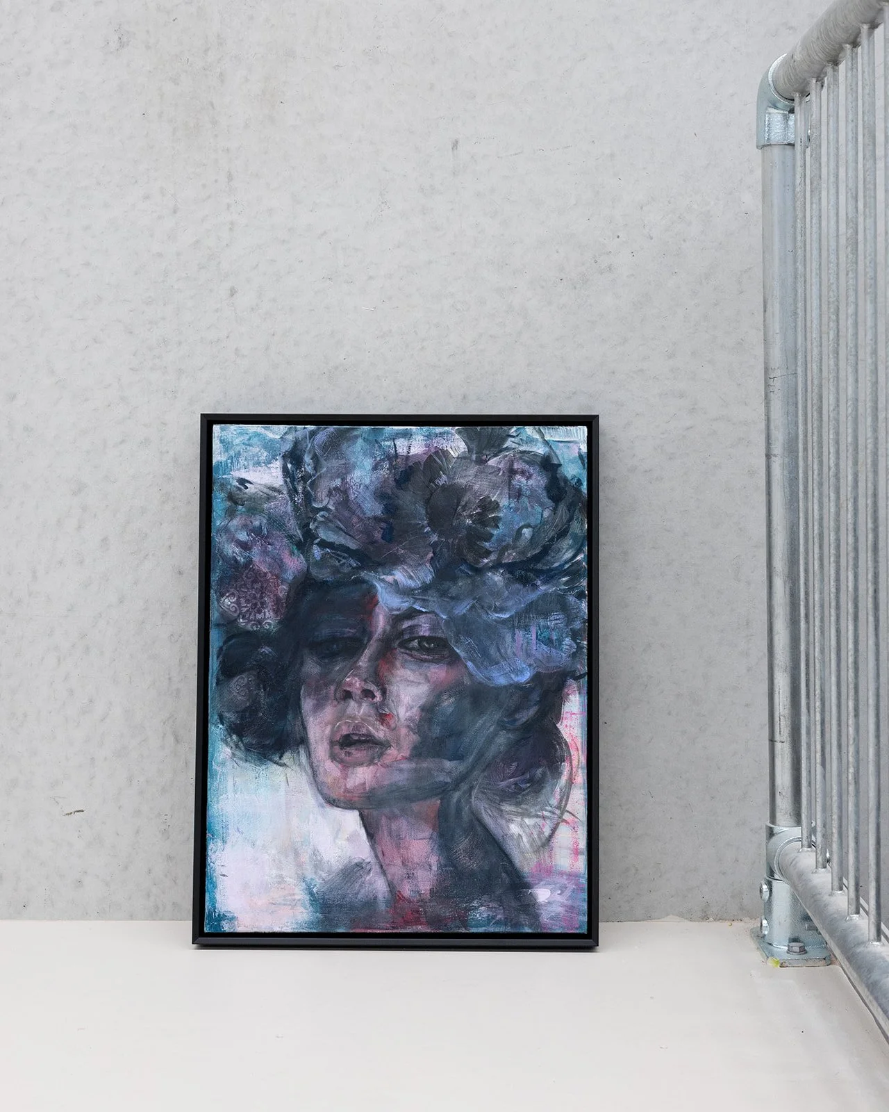 Framed abstract portrait of a woman with large hat, leaning against a plain wall near a metal railing.