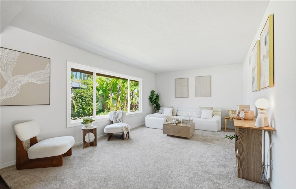 Sculptural chairs and a low oak table hold the center of the room without blocking the picture window, which frames the mature tropical planting and pulls the backyard into the space. Restrained artwork and a warm wood console along the far wall add 