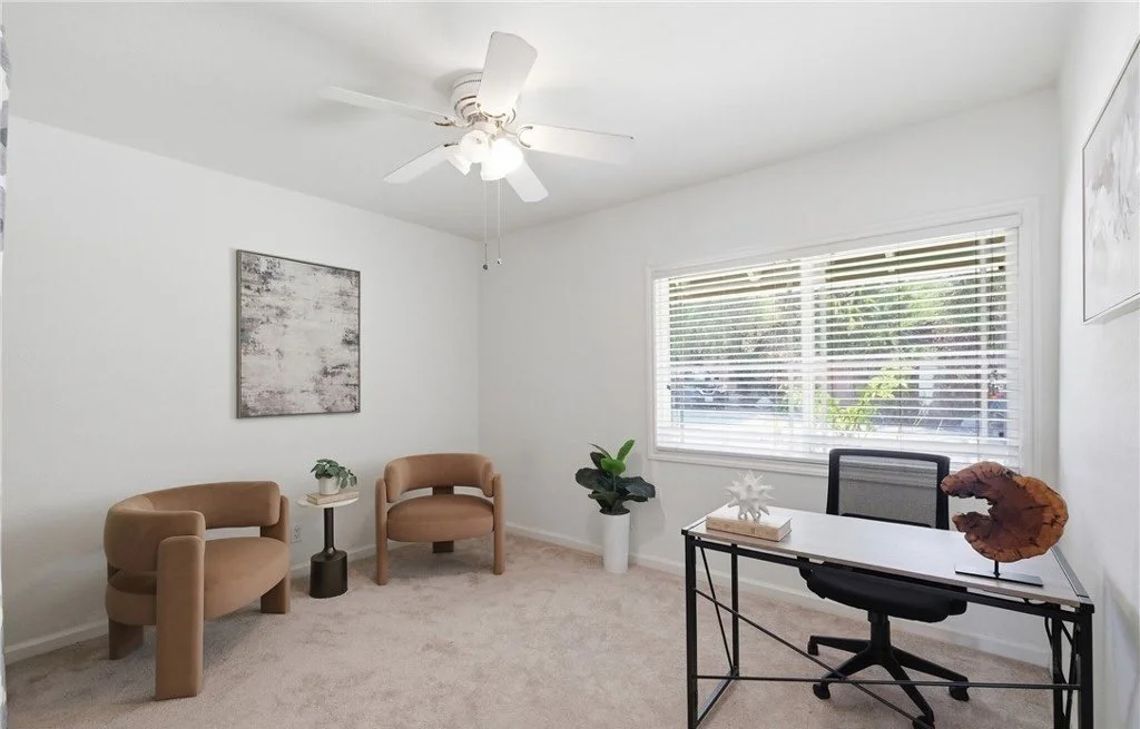 Staged as a flexible home office, this room pairs a slim black-frame desk with two curved lounge chairs so buyers can see it working as a workspace and a sitting room at once. Keeping the furniture low and the center of the floor open makes the squar