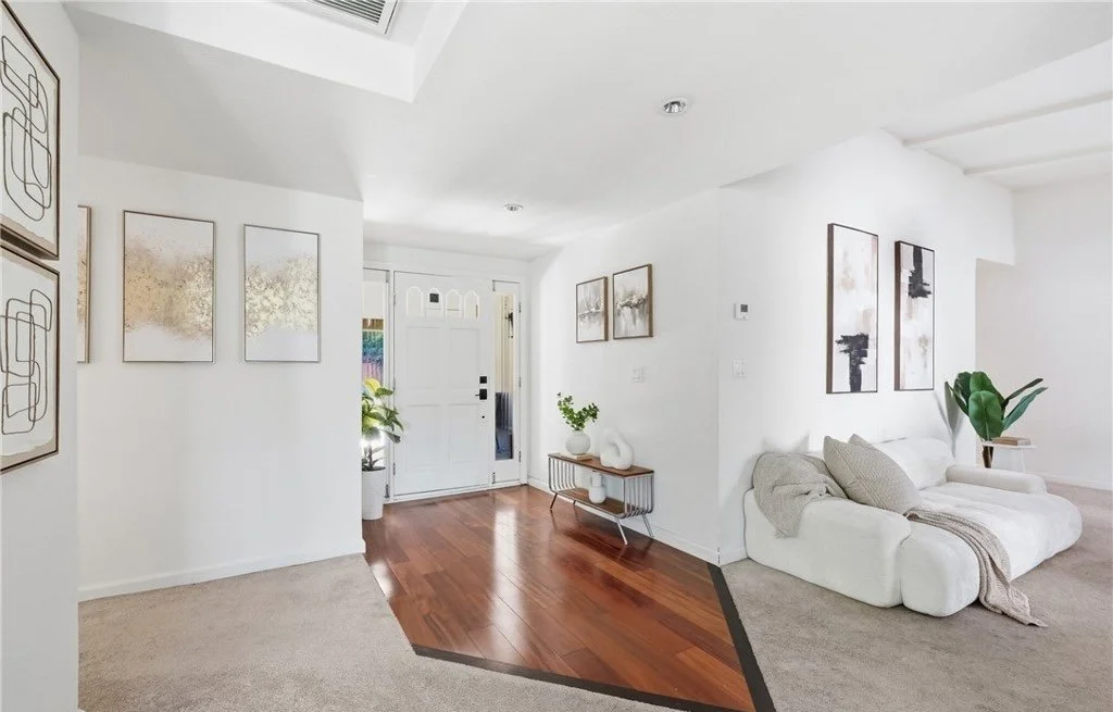 The inlaid hardwood entry is left deliberately uncluttered, with a low dark cherry console chosen to pick up the tone of the floor and a symmetrical run of framed art guiding the eye toward the living space. A boucle sofa at the edge of the frame mar