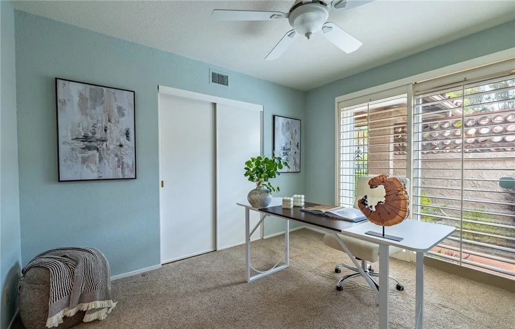 The third bedroom is staged as a home office with a glass-topped desk that takes up almost no visual space, so buyers register the room's square footage rather than the furniture in it. The teal wall is left as the only strong color in the house, whi