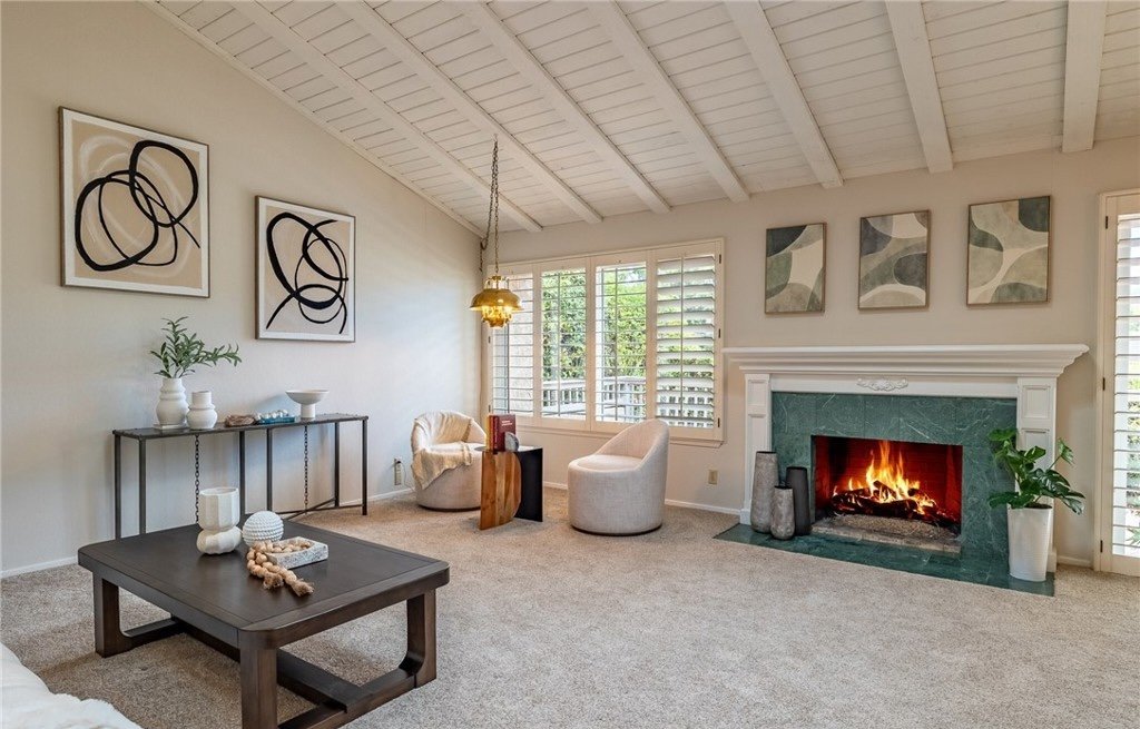 The green marble fireplace is the room's one piece of real character, so the staging keeps everything around it low and neutral and lets it hold the center of the frame. A trio of muted canvases above the mantel and a console against the far wall add