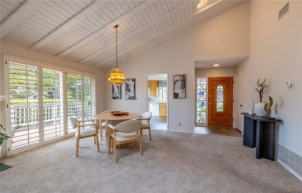 From the entry, the dining table, the kitchen pass-through, and the balcony doors are all visible at once, which is the clearest evidence of how open this floor plan actually is. The console and sculpture by the door give arriving buyers something fi