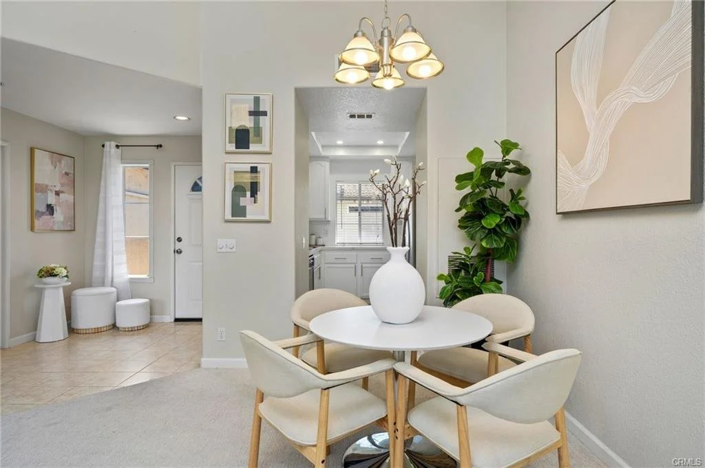 Sculptural furnishings, warm wood accents, and a statement chandelier create an intimate dining area with a clean, modern aesthetic. The restrained palette keeps the space feeling open while giving it a distinct sense of refinement