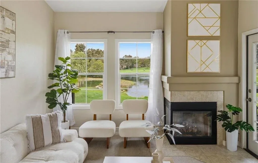 A pair of low boucle chairs and an ottoman sit square to the window rather than the fireplace, so the greenbelt and the water are the first thing you see from the sofa. Nothing on this side of the room rises above the sill, which leaves the light and