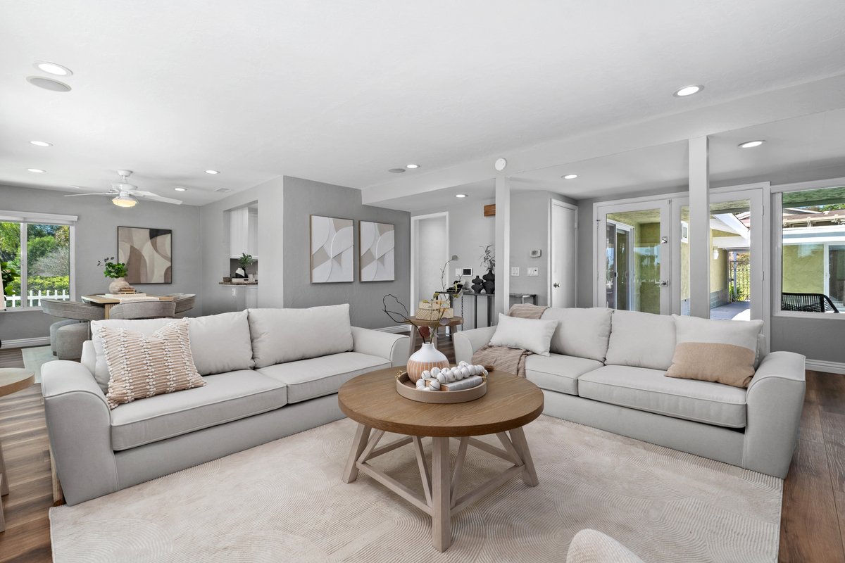 From the far end the same room has to hold a long sightline through to the dining area and out to the patio doors. Two matching sofas face each other across a round oak table to give the space a centre, and the framed art is hung at one height so the