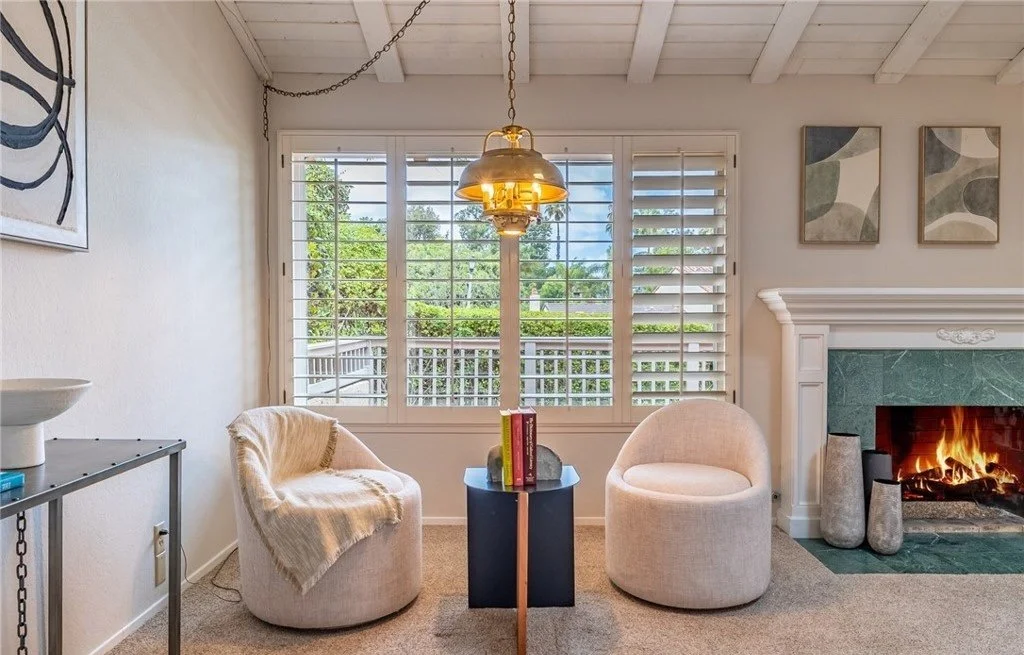 Two swivel chairs and a slim drink table turn the corner beside the fireplace into a place to actually sit, rather than the pass-through it would otherwise read as. Keeping the pair low and armless preserves the view through the plantation shutters t