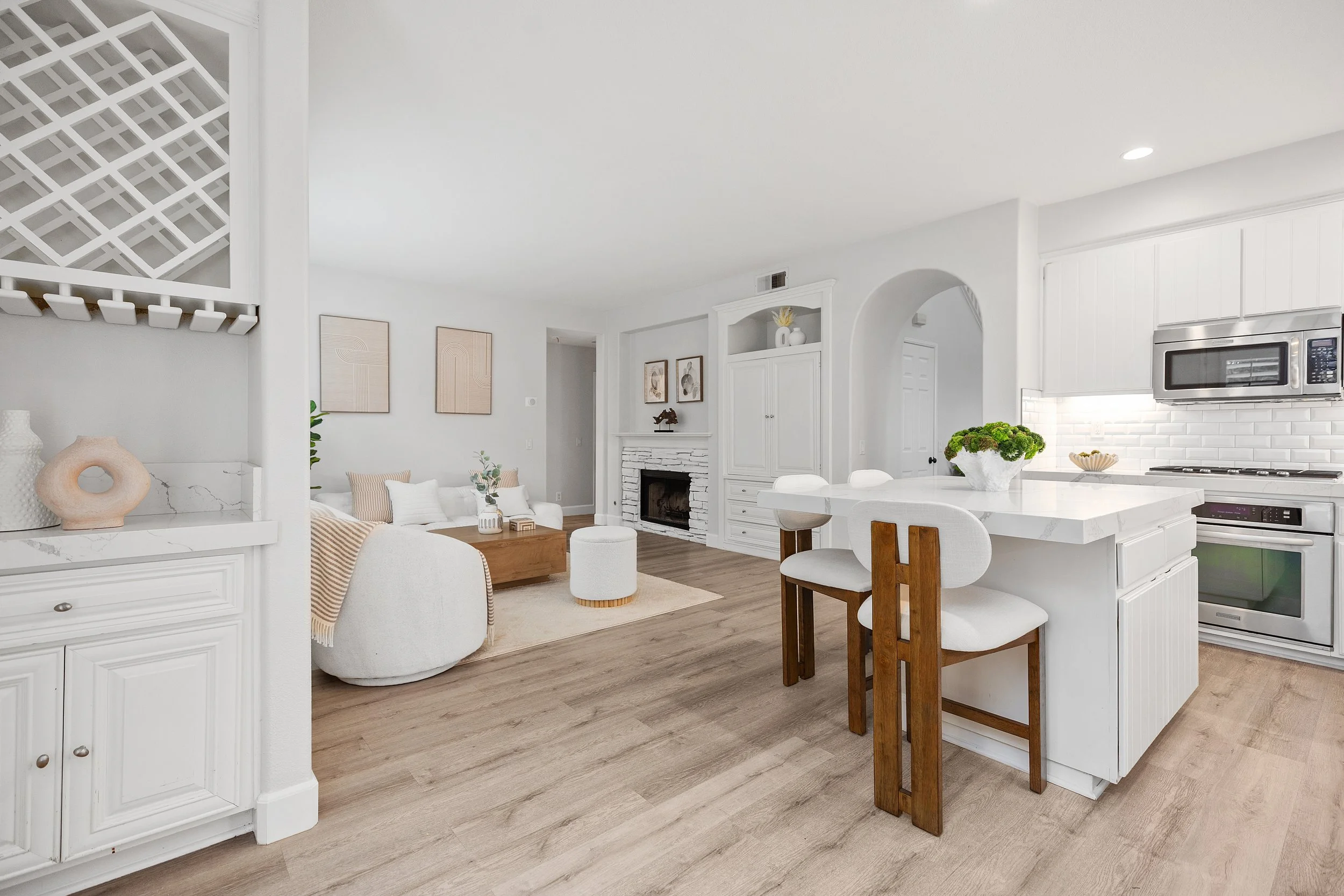 Bright, modern open-concept living room and kitchen with white cabinetry, a white brick fireplace, and light wood flooring.
