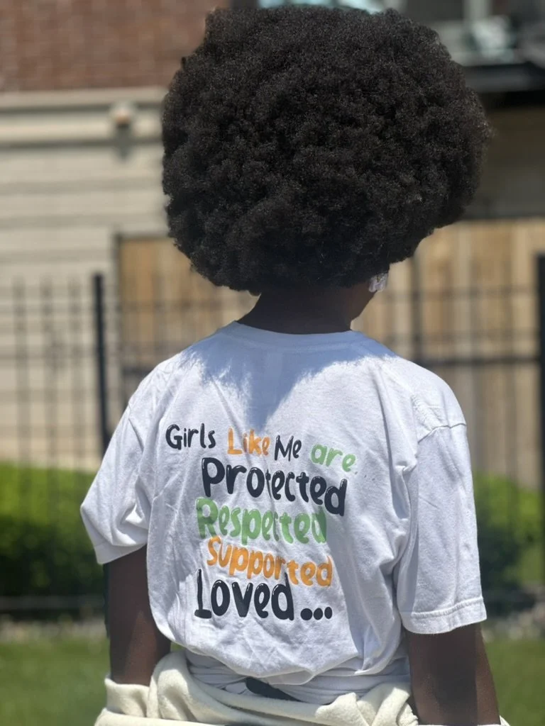 Girl showing the back of her shirt that says, "Girls like me are protected, respected, supported, loved..."