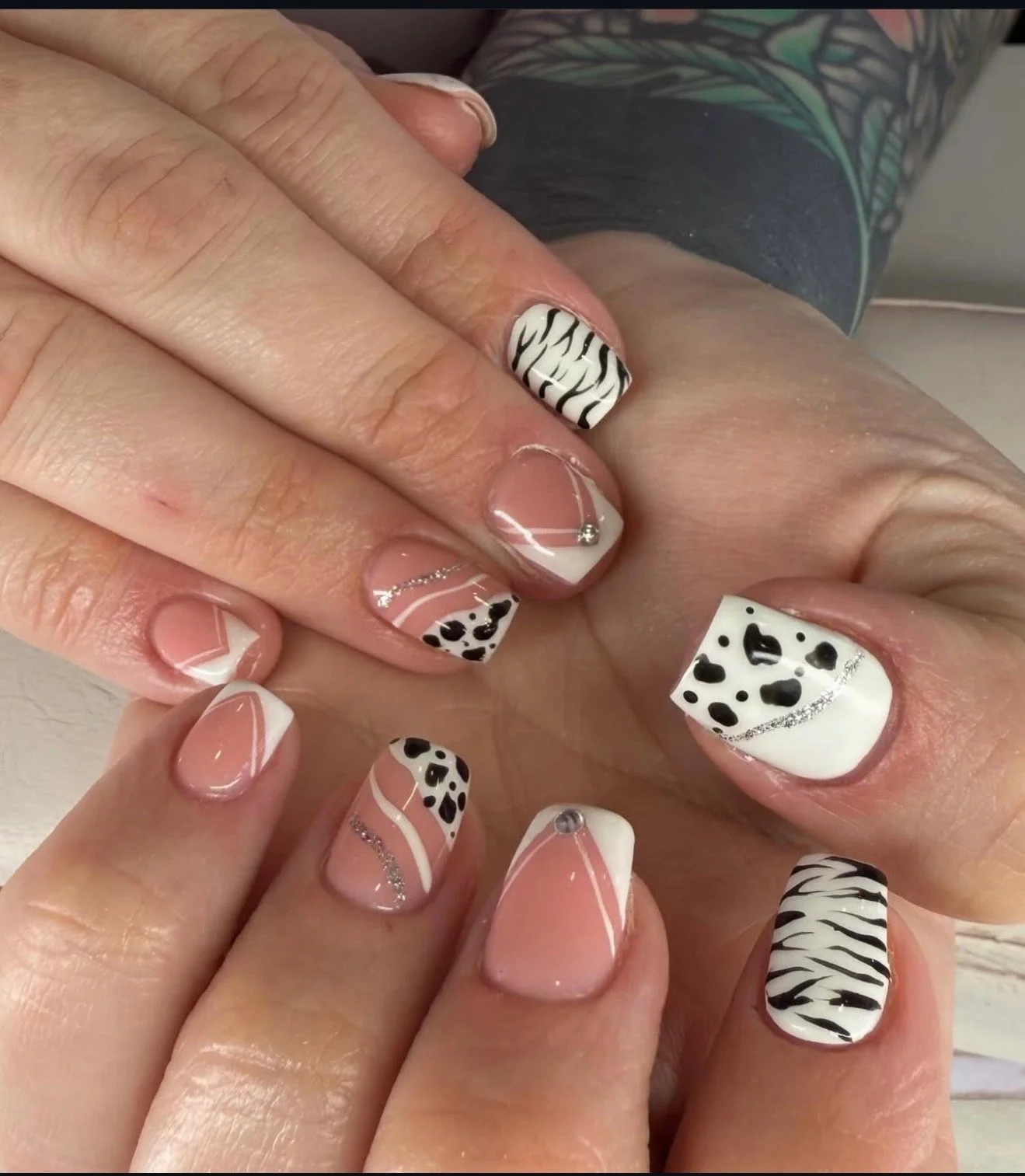 Close-up of hands showing manicured nails with a zebra and cow print design, rhinestones, and white and black accents.