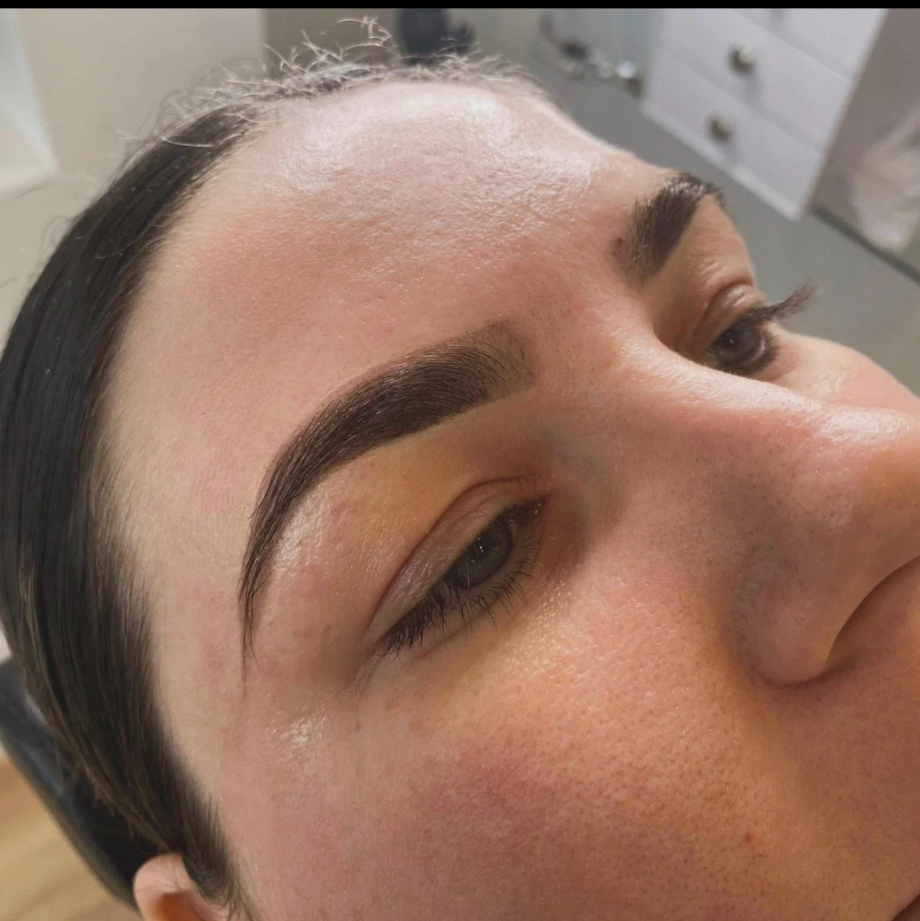 Close-up of a woman's face showcasing freshly done eyebrow microblading or eyebrow tattooing, with smooth skin and well-shaped eyebrows.