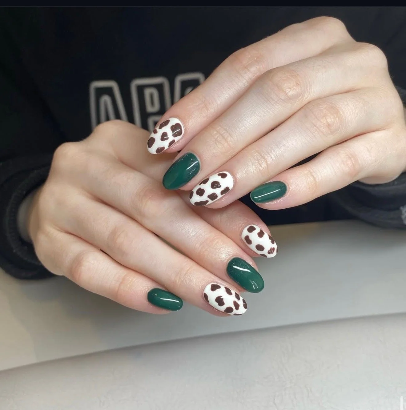 Close-up of a person's hands with manicured nails, featuring green polish on some nails and a white base with brown leopard print on others.