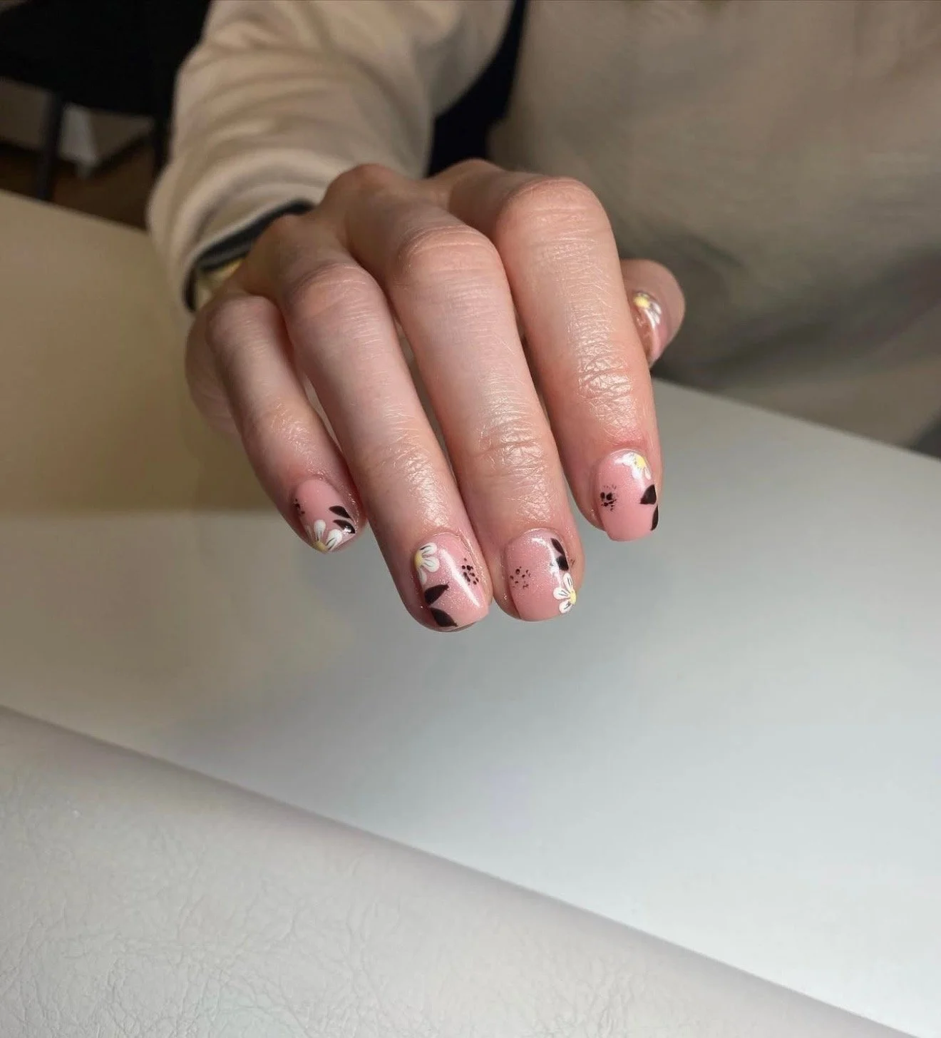 Close-up of a person's hand with decorated nails featuring floral and abstract designs on a pink base.