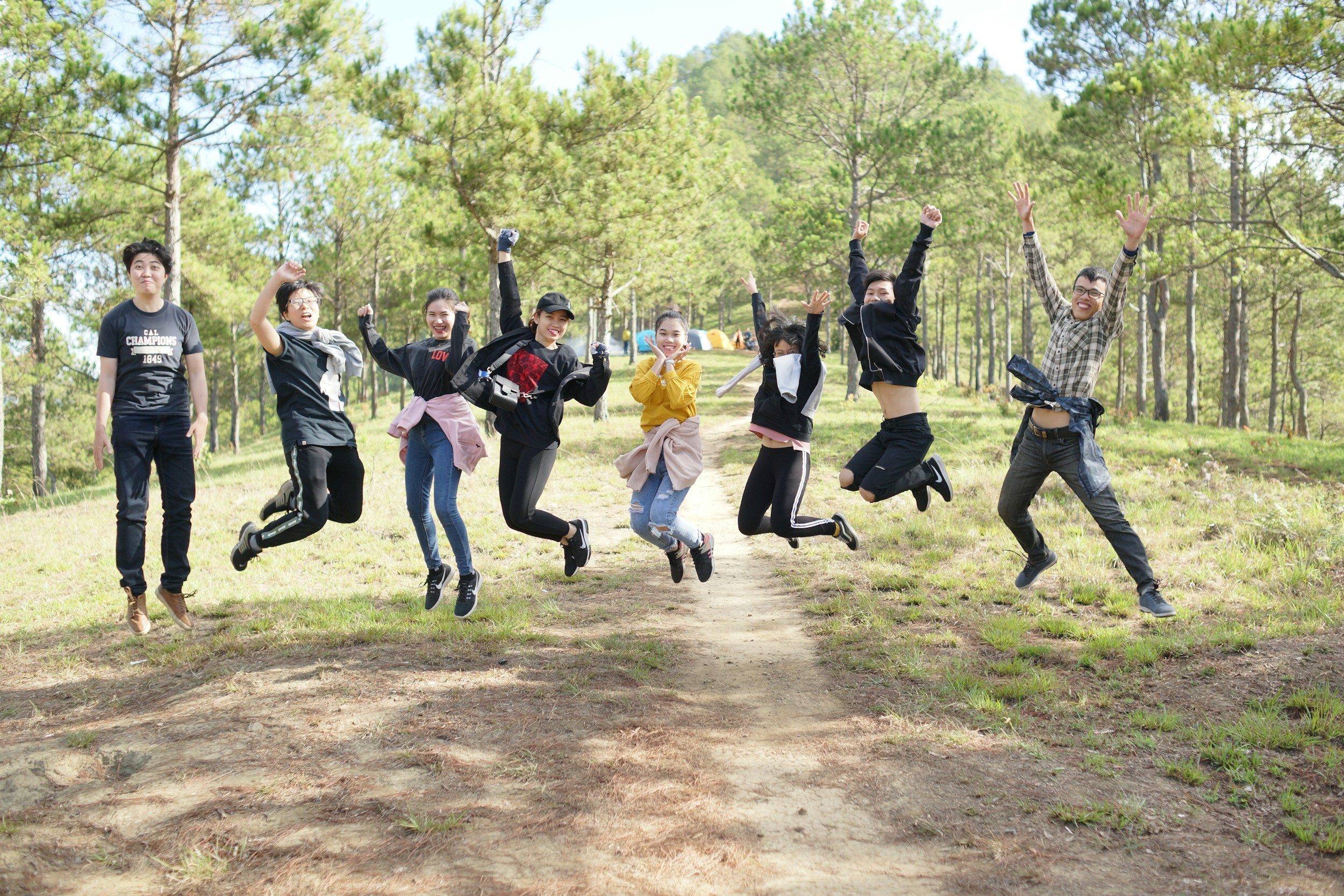 Group of friends jumping in the air on a forest trail during daytime.