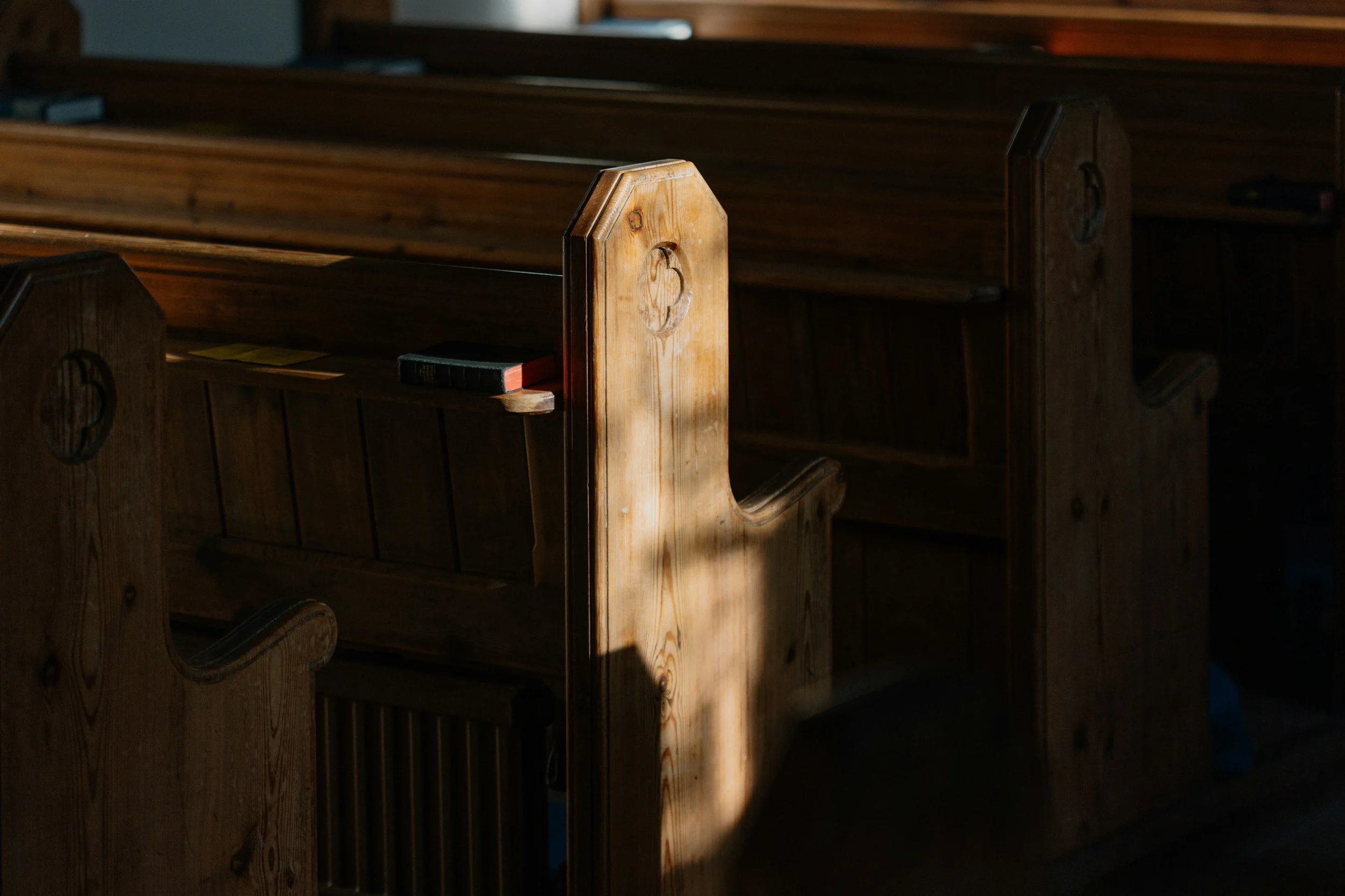 Wooden church pews with a small book resting on the armrest, dimly lit.
