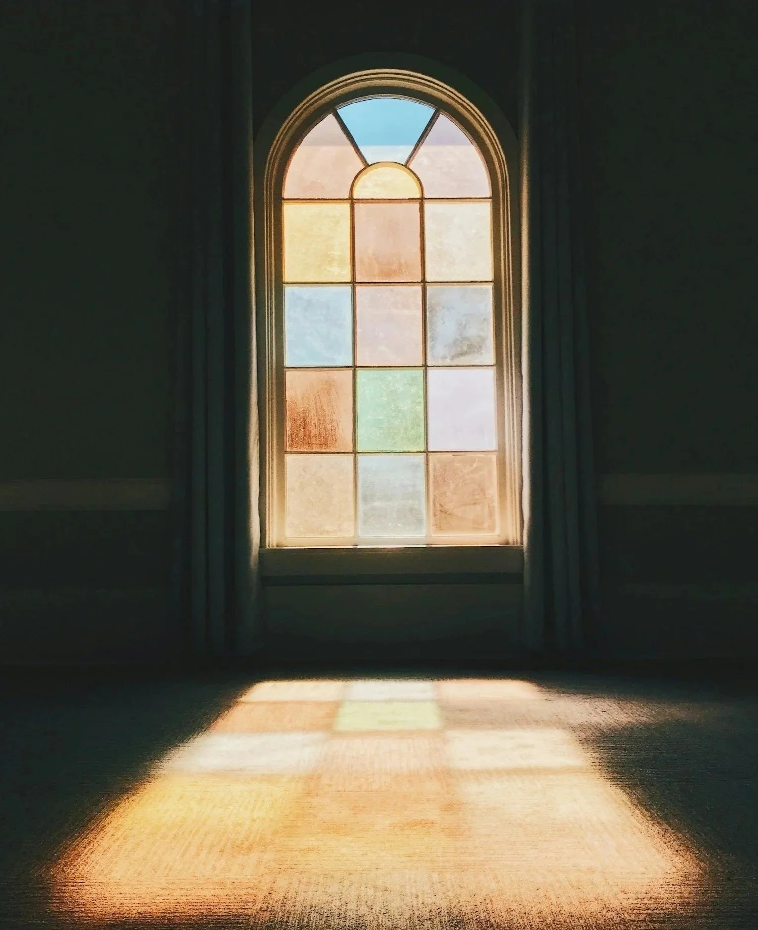 Sunlight coming through stained glass window illuminating a wooden floor.