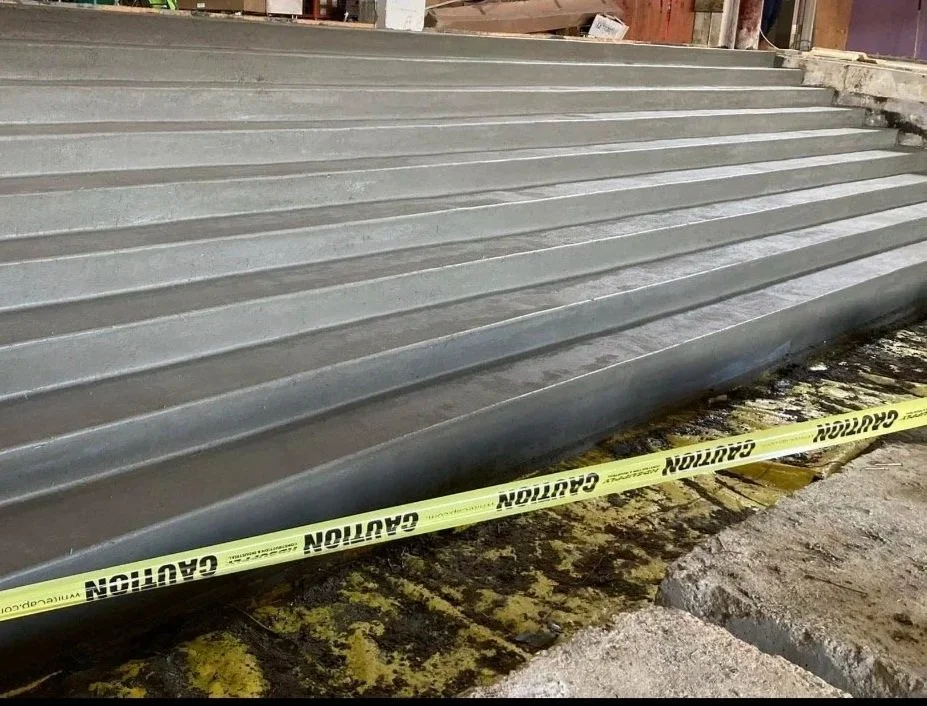 Metal ramp with yellow caution tape in front of a construction site.