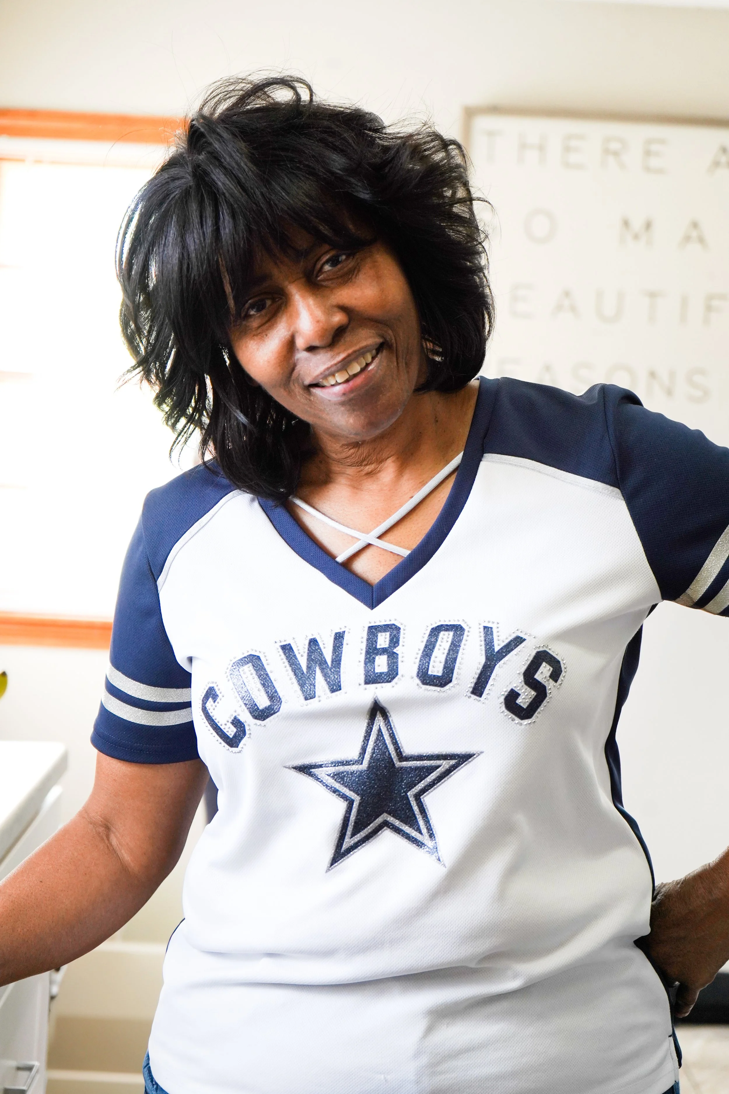 Woman wearing a Dallas Cowboys football jersey smiling at the camera in an indoor setting.