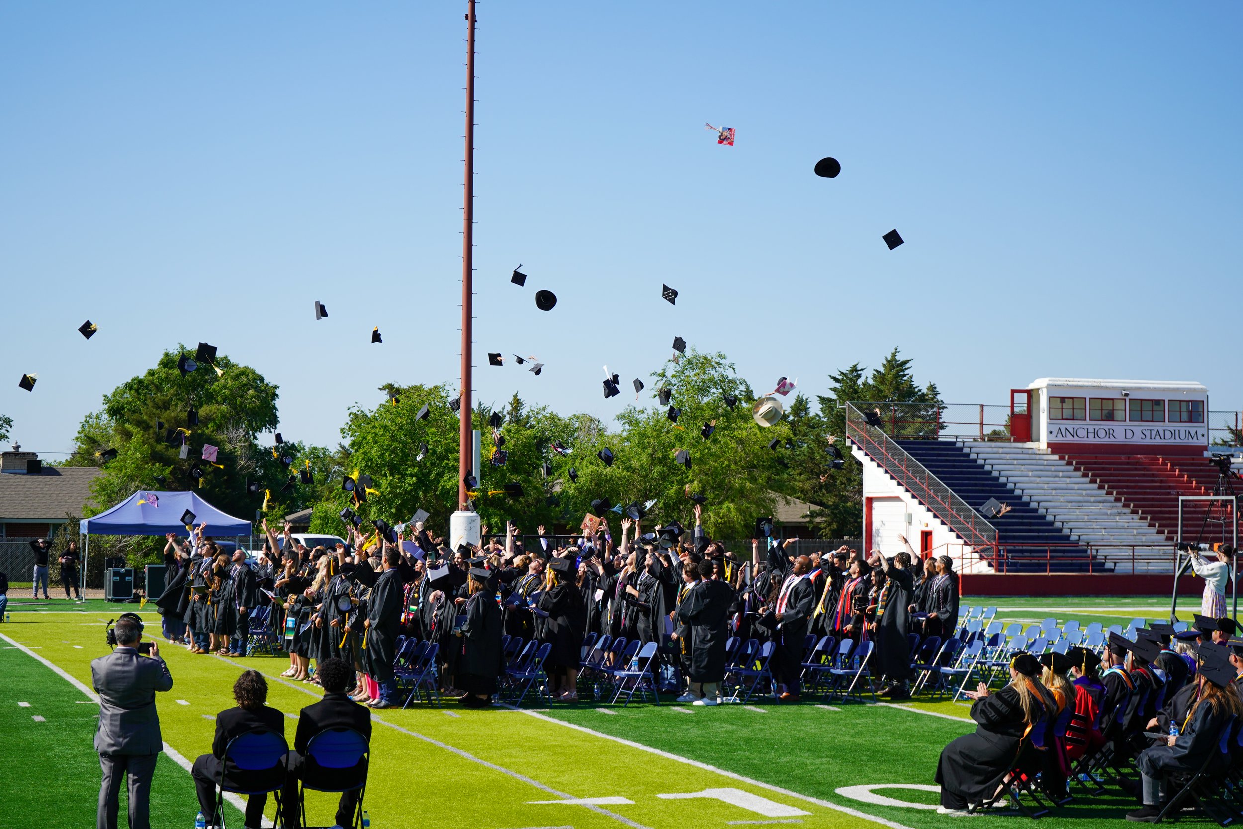 Graduates throwing caps in the air on a sports field during a graduation ceremony.