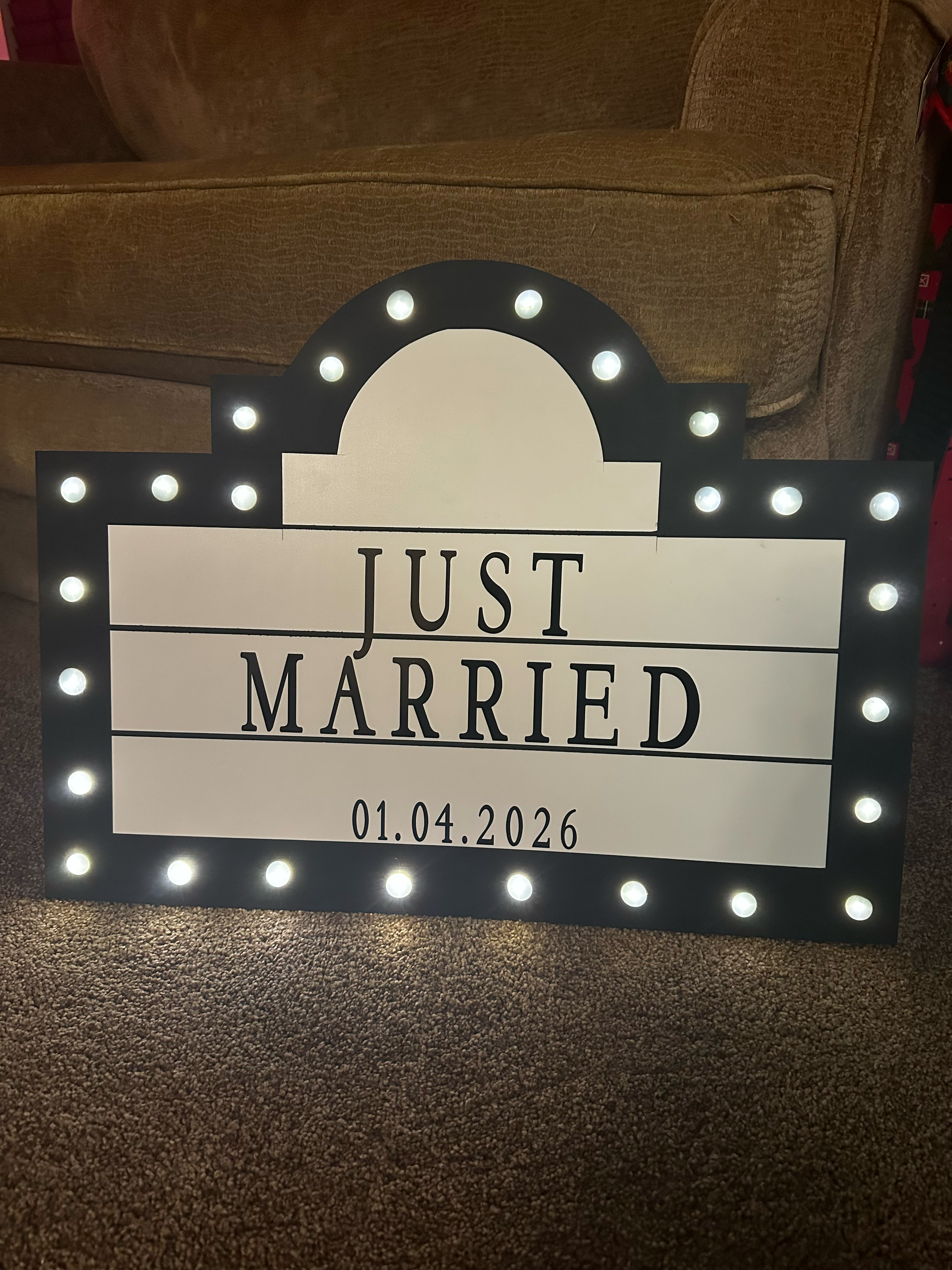 Light-up welcome sign reading "Just Married" on April 26, 2026, with black text on a white background and decorative lights around the border.
