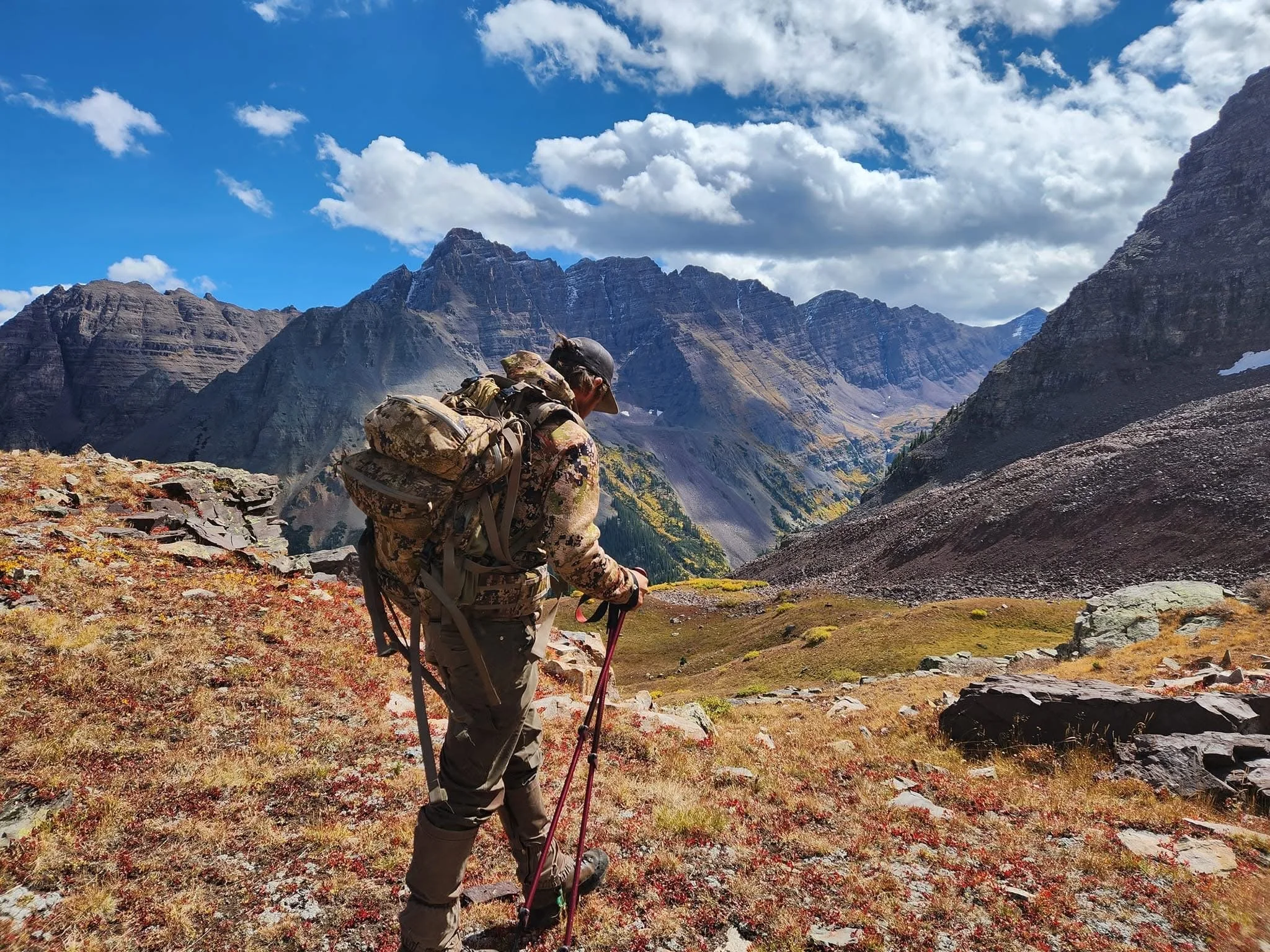 A person hiking in a mountainous landscape with rugged peaks and partly cloudy blue sky.