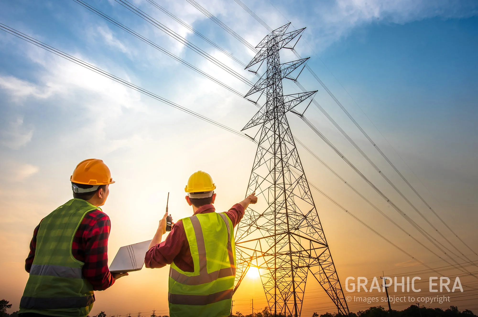 Two electrical workers wearing safety vests and helmets inspecting a power transmission tower at sunset.