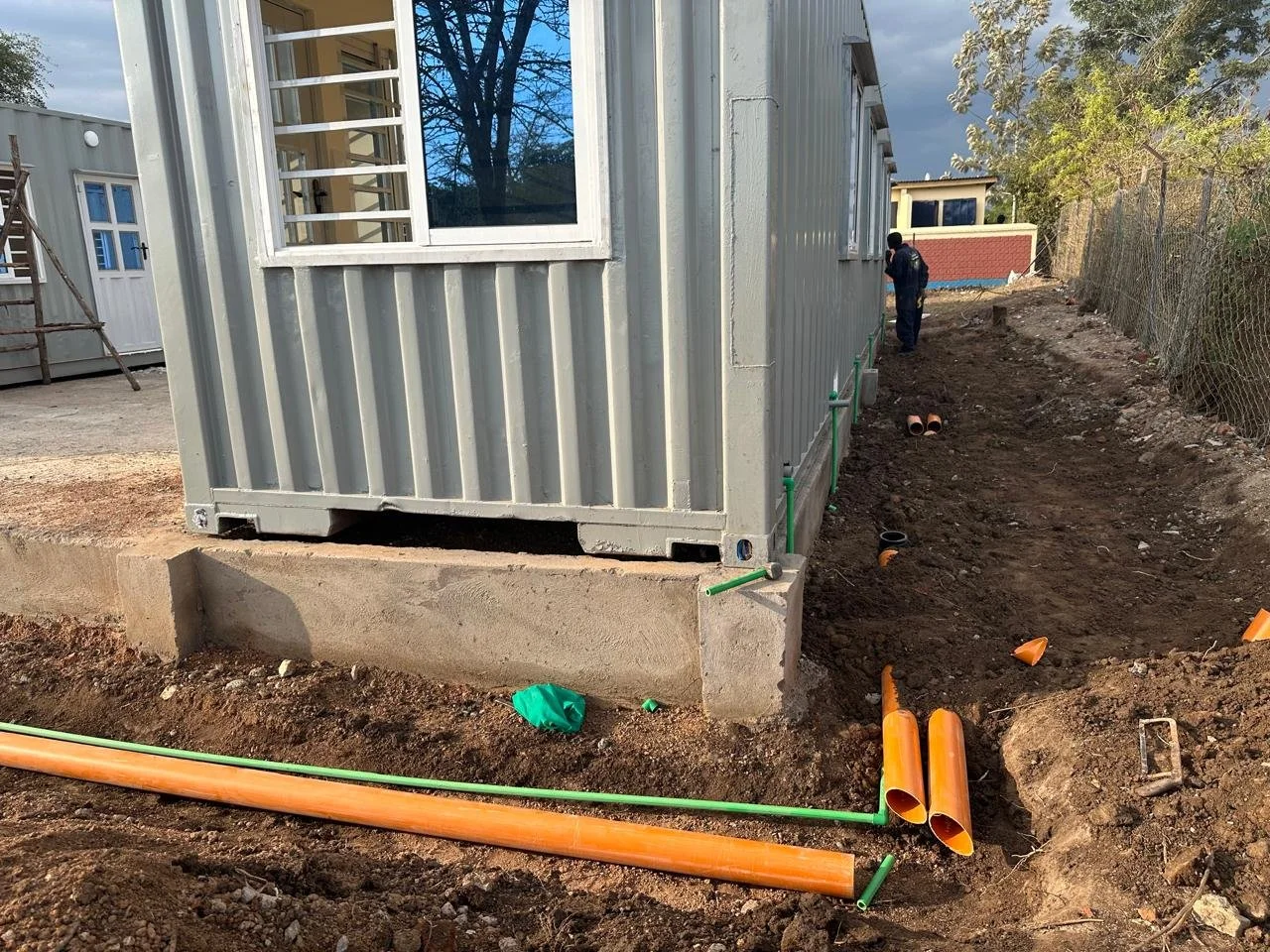 Pipes in the ground surrounding a shipping container.