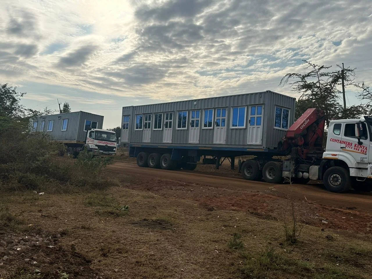 Two large trucks transporting two shipping containers.