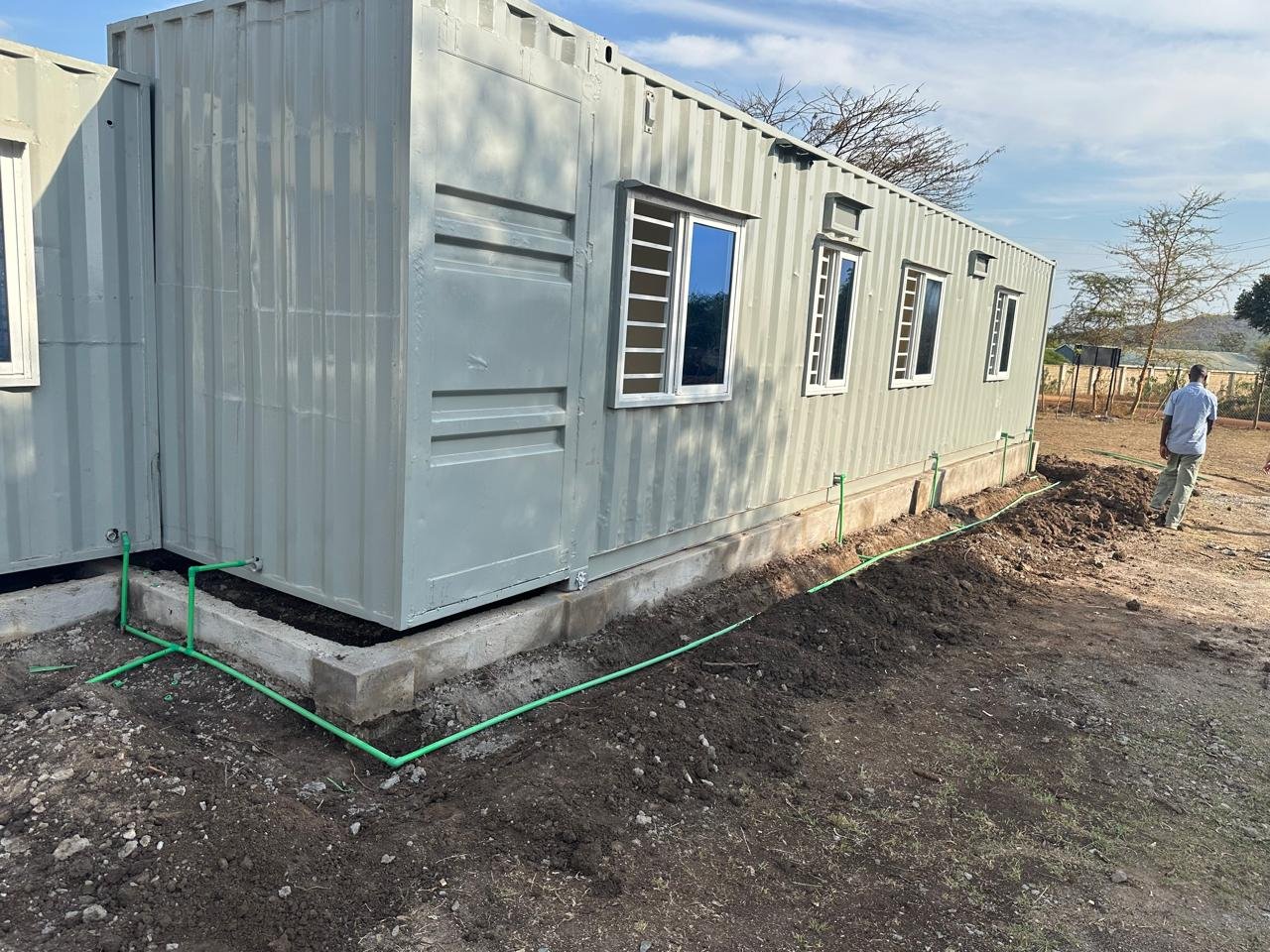 Exterior of a shipping container showing green pipes attached for plumbing.