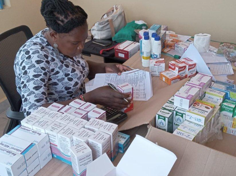 Woman organizing and counting various pharmaceutical medications on a desk, with boxes and bottles of medicine around her.