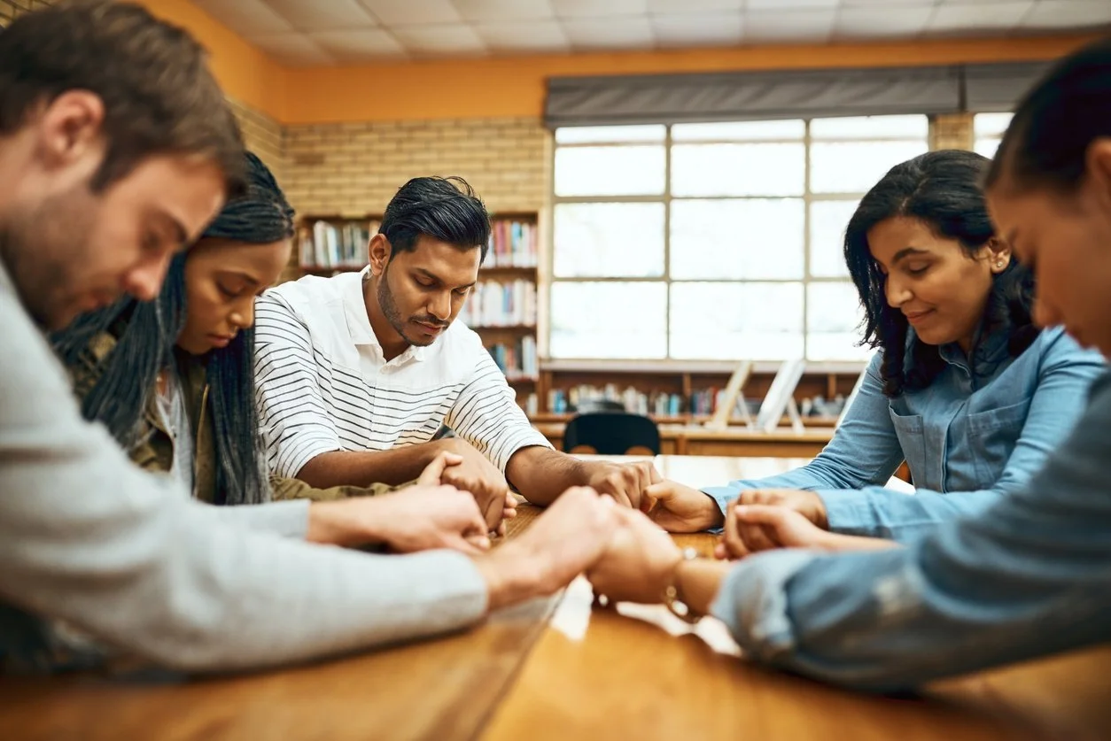 Faith and spirituality - A group of diverse individuals holding each other's hands while praying.