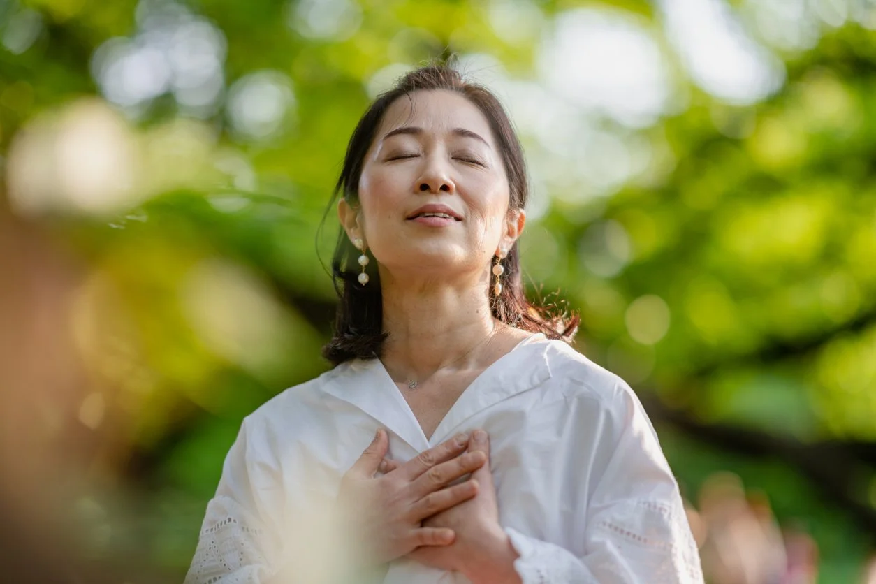 Faith and spirituality practices - A woman standing outside with her hands over her heart.