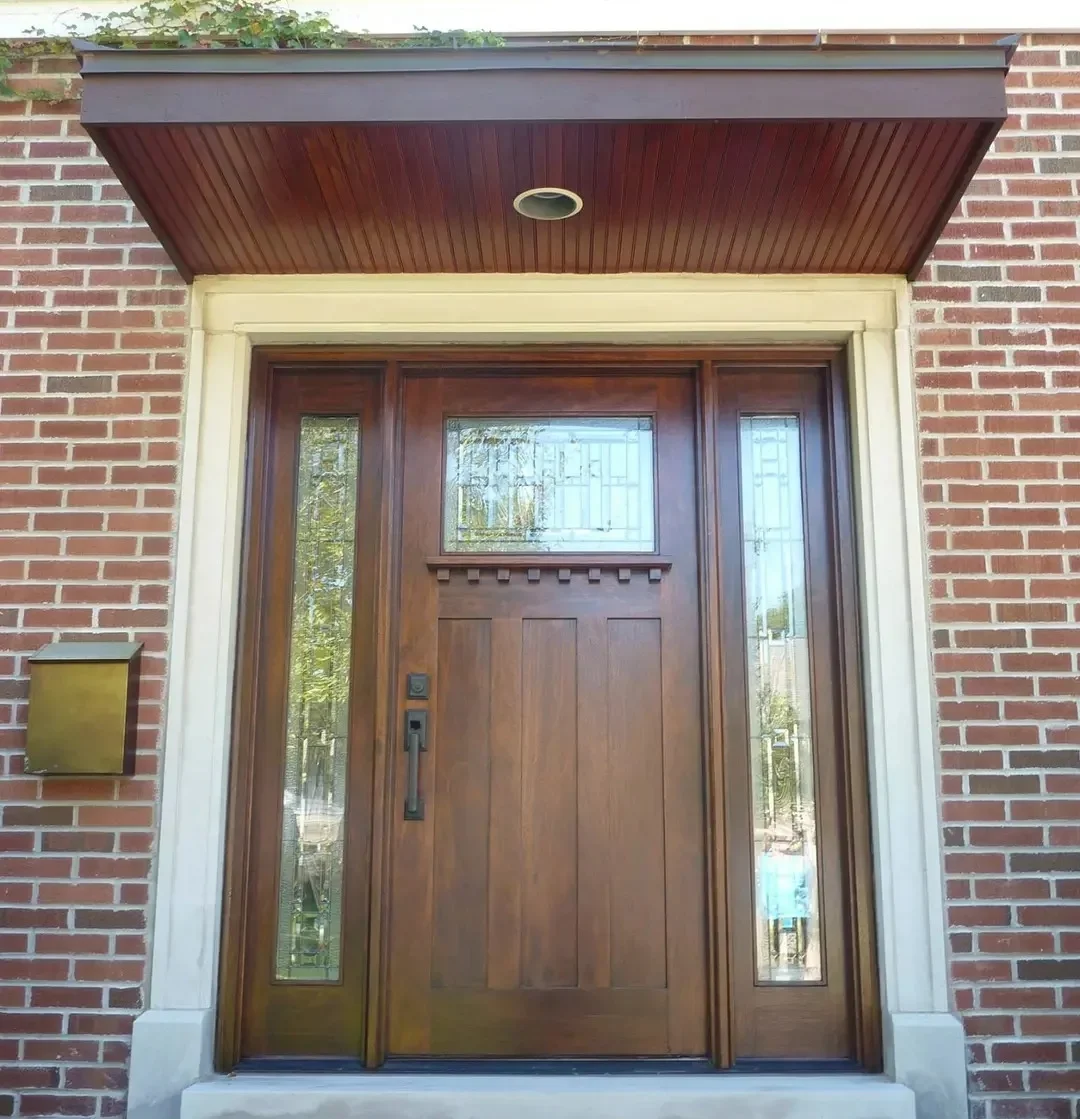 Re-stained door entrance with lighter brown Wooden front door with glass panels on each side and a small window above, set in a brick wall.