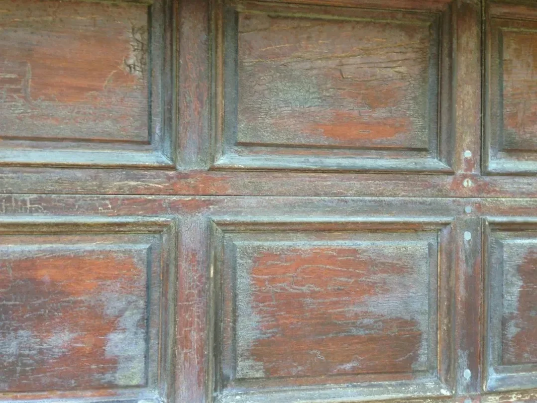 Close-up of an old, weathered wooden door with peeling reddish-brown paint and visible cracks.