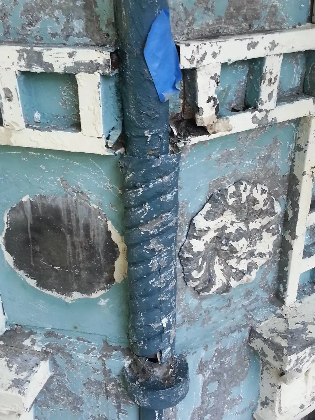 Close-up of a damaged exterior wall with cracked paint and missing spiral pipe decorative items prior to of a construction or renovation site.