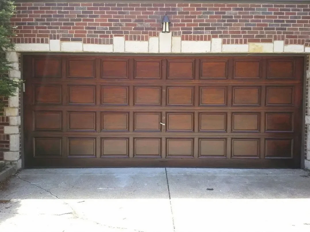 Restored with stain wooden garage door with brick and stone exterior, single handle in the middle, and a small exterior light above.