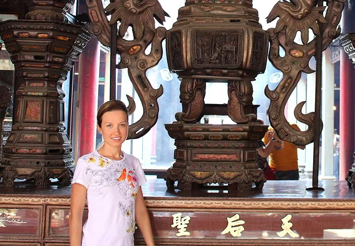 A woman standing next to an ornate, carved wooden altar with intricate decorations, including dragon motifs, inside a building with large windows.
