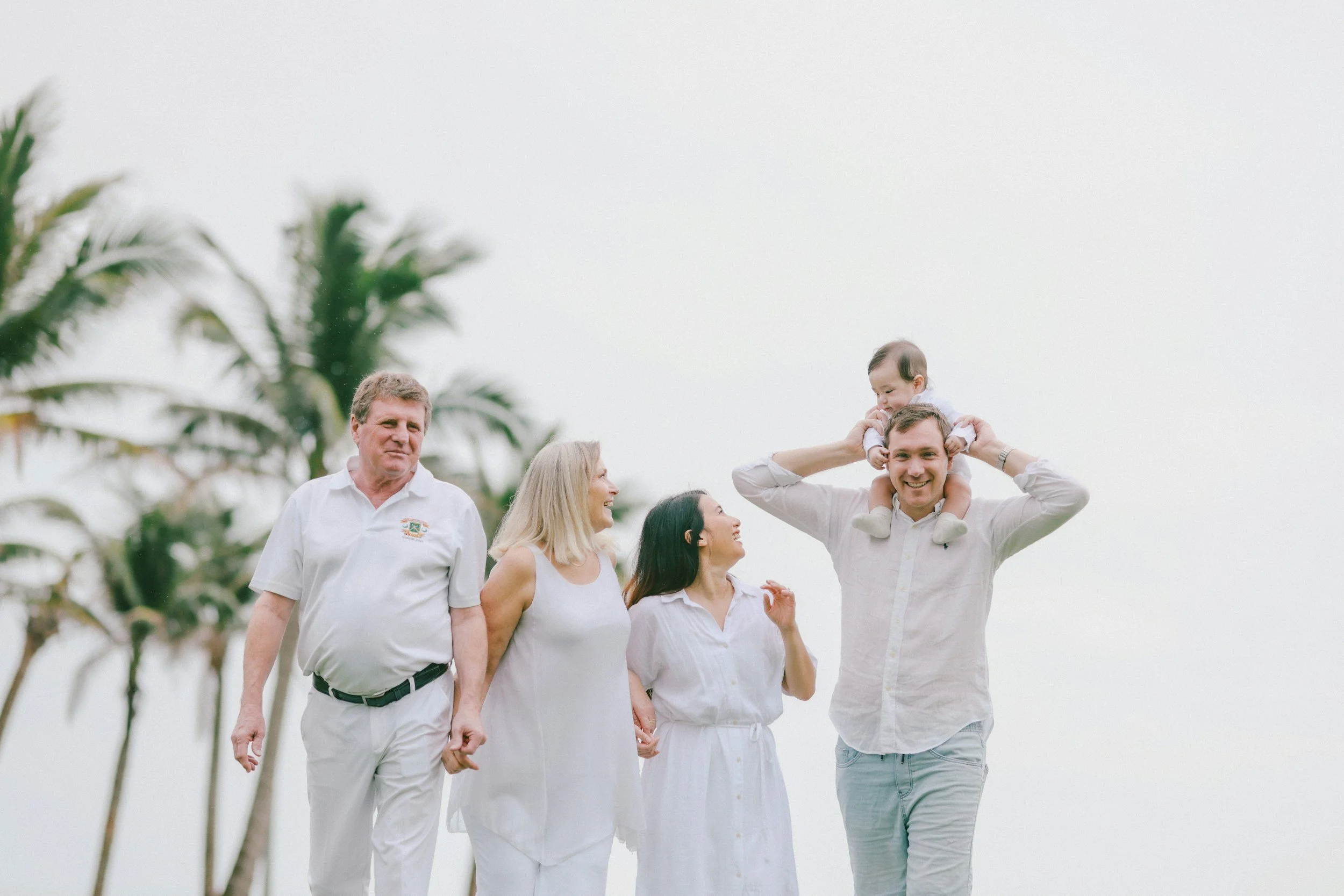 Family holding hands and walking outdoors with palm trees in the background, enjoying a sunny day.