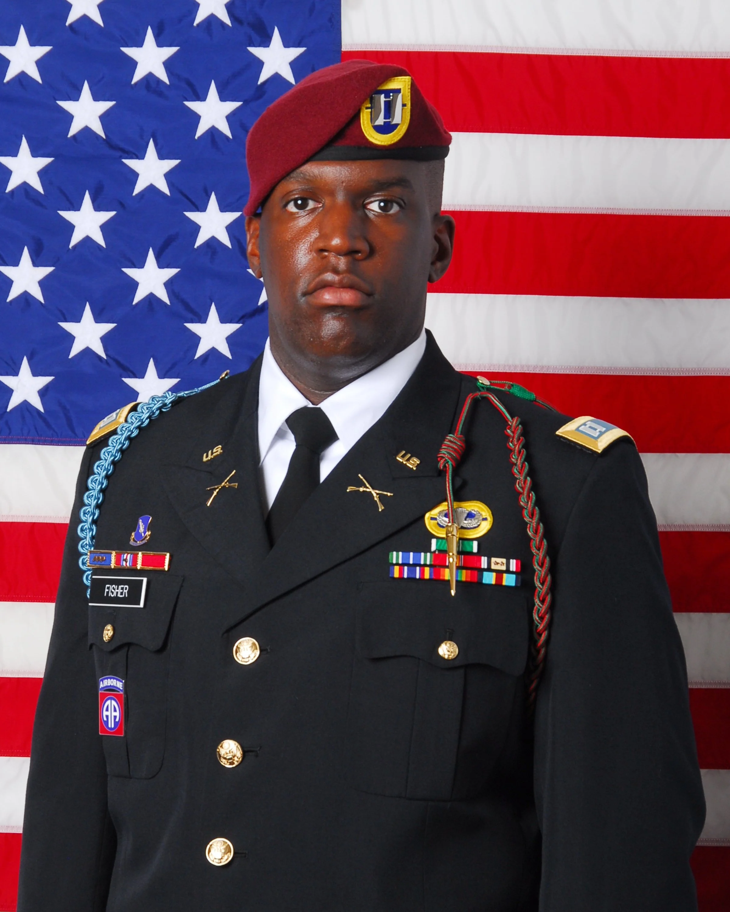 A soldier in dress uniform standing in front of an American flag.