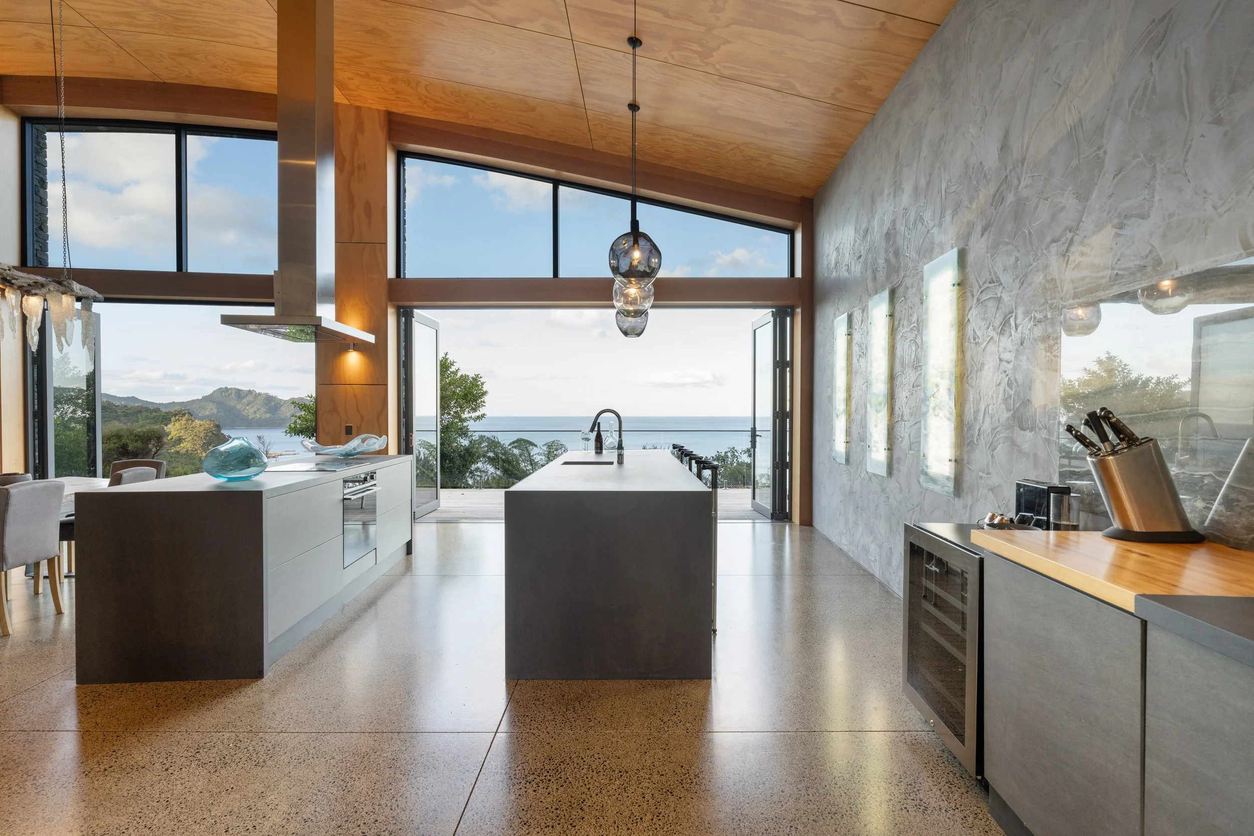 Modern kitchen with large windows and ocean view, featuring a central island, pendant lighting, and minimalist cabinetry.