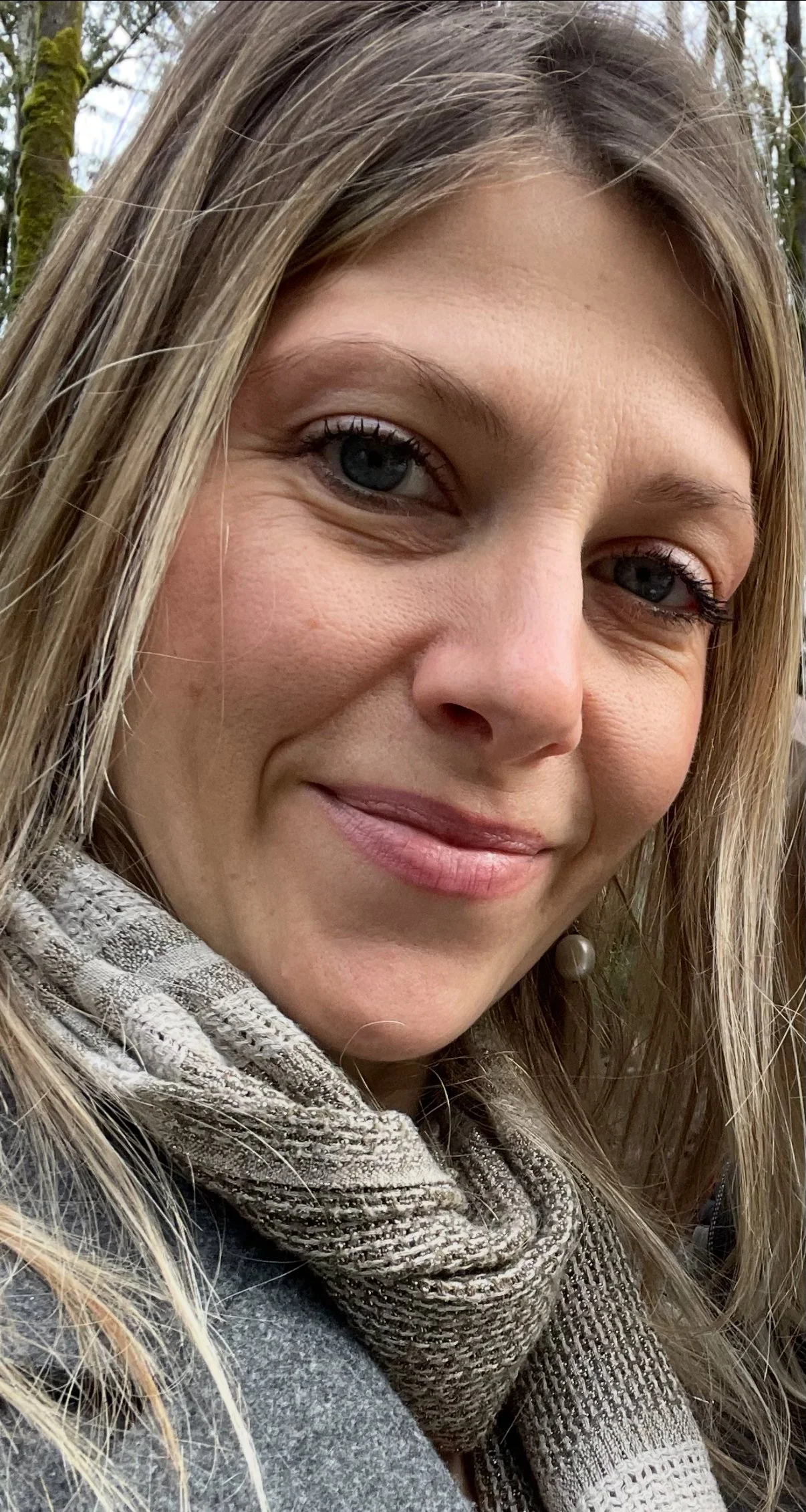 Close-up of a smiling female Canadian Financial Broker with blonde hair, blue eyes, wearing a scarf and gray coat outdoors.