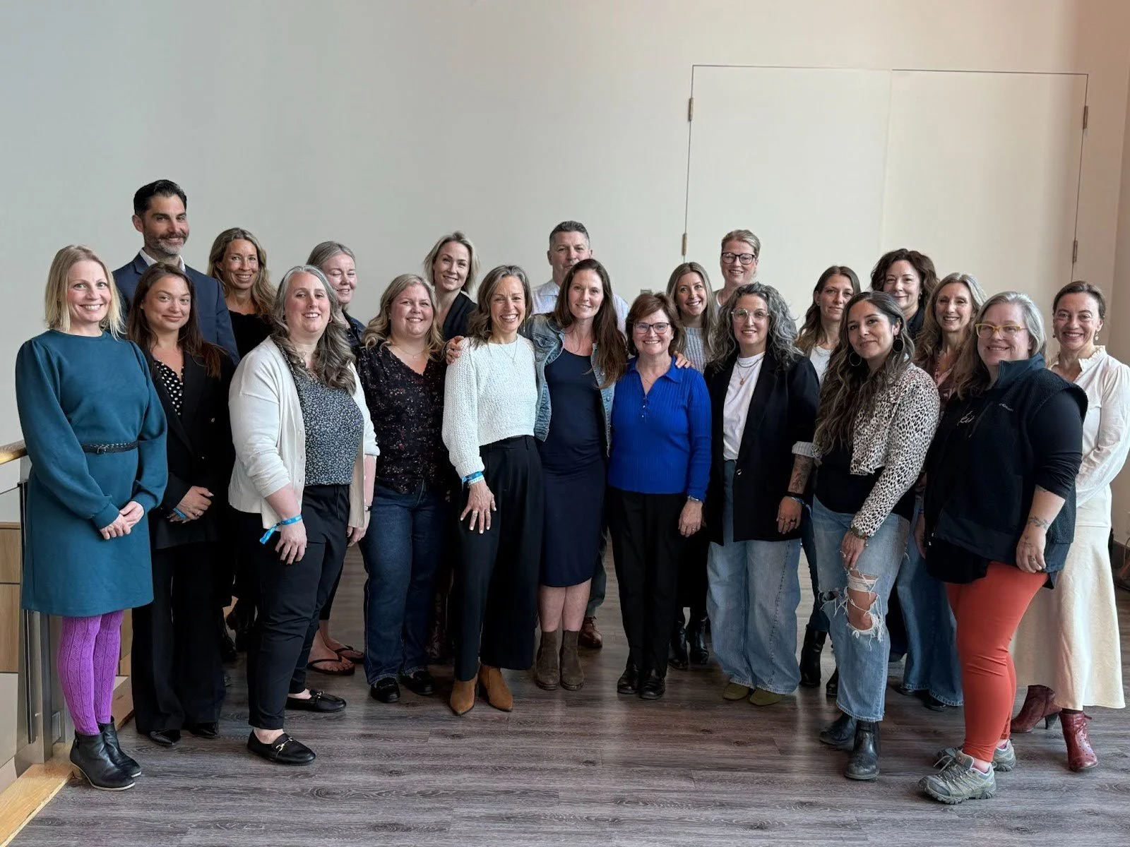 A diverse team of Financial Strategists in Canada, comprising of 22 diverse women and one man standing together in an indoor venue, smiling for a group photo.