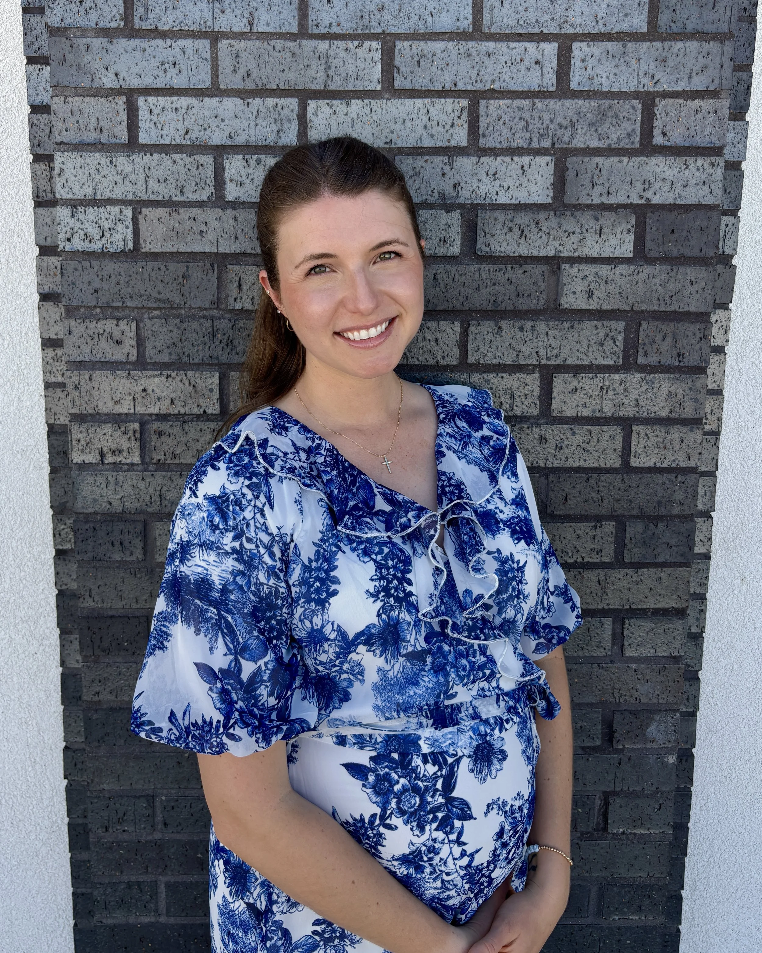 This is a photo of Amelia Rauch, a veterinarian in Boerne, Texas posing in front of a dark brick wall and wearing a blue and white dress.
