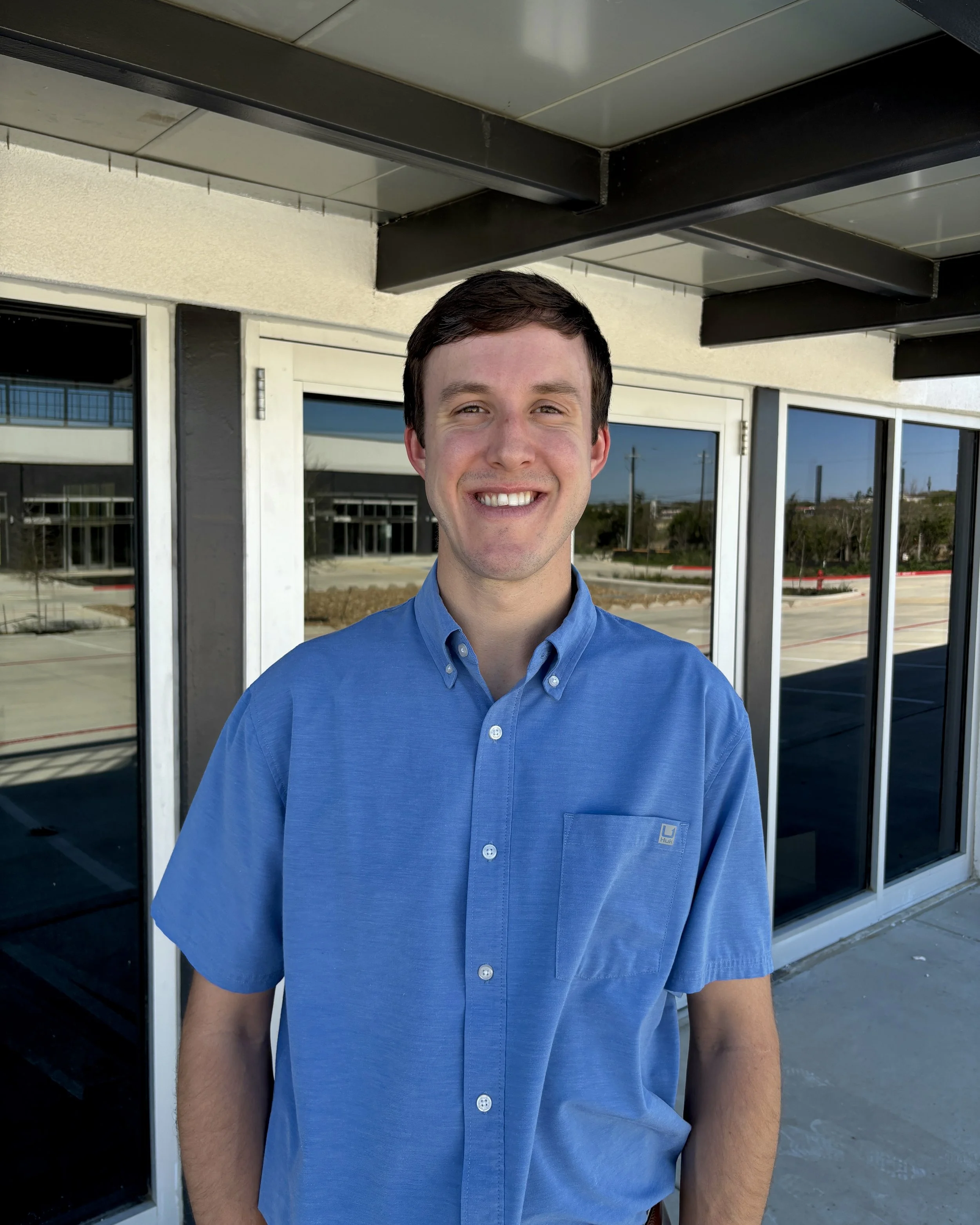 This is a photo of Mike Rauch, a veterinarian in Boerne, Texas, posing in front of glass windows and wearing a blue button-down shirt.