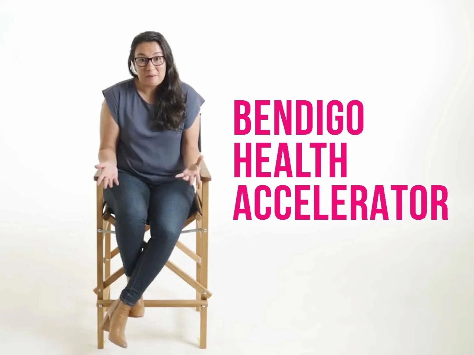 Woman with glasses seated on a wooden chair in front of a plain white background. Text on the right reads, 'Bendigo Health Accelerator' in bold magenta font.
