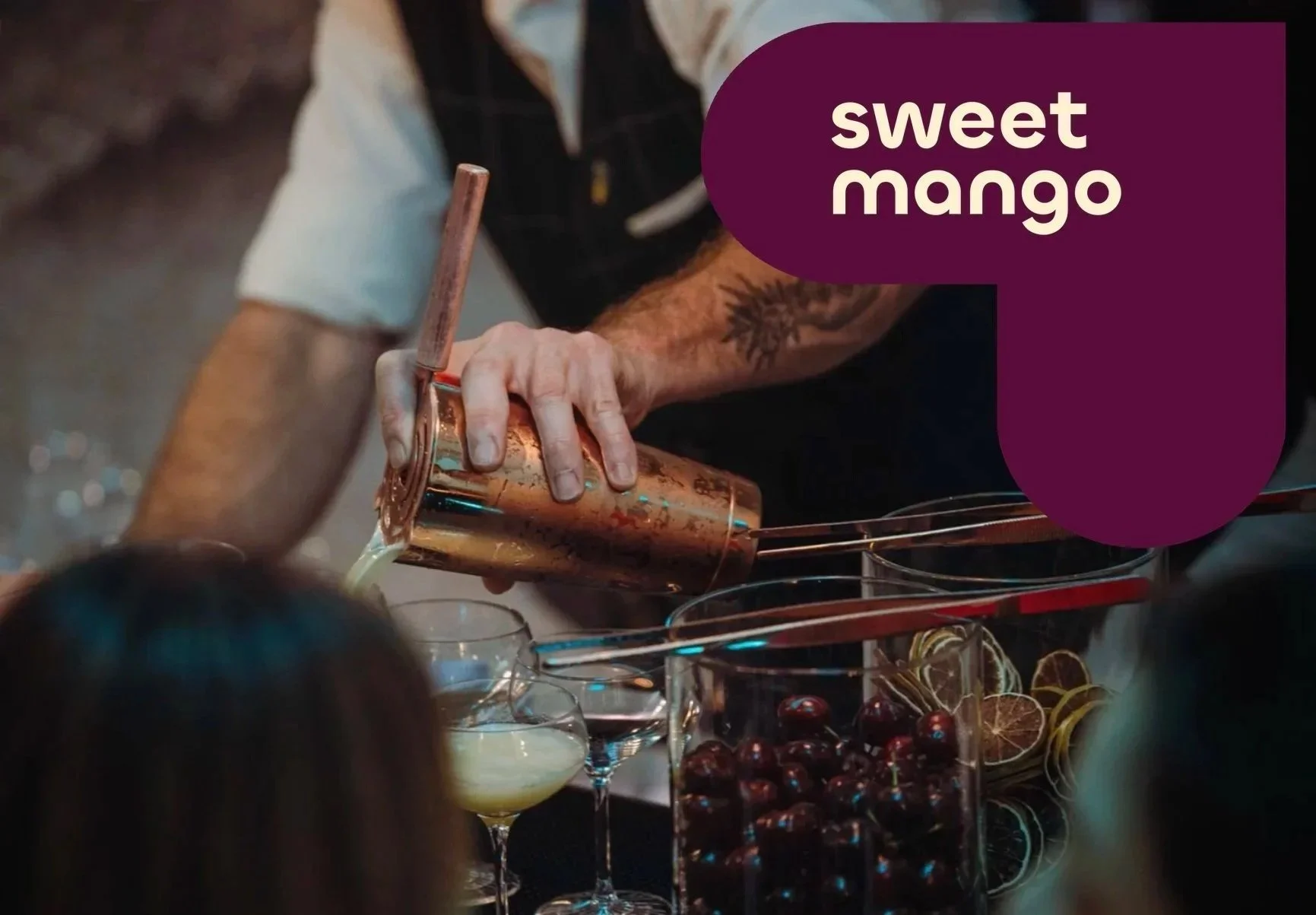 A bartender pours a creamy cocktail from a copper shaker into a glass, with a crowd of people and a drink display in the background. The scene is labeled 'sweet mango.'
